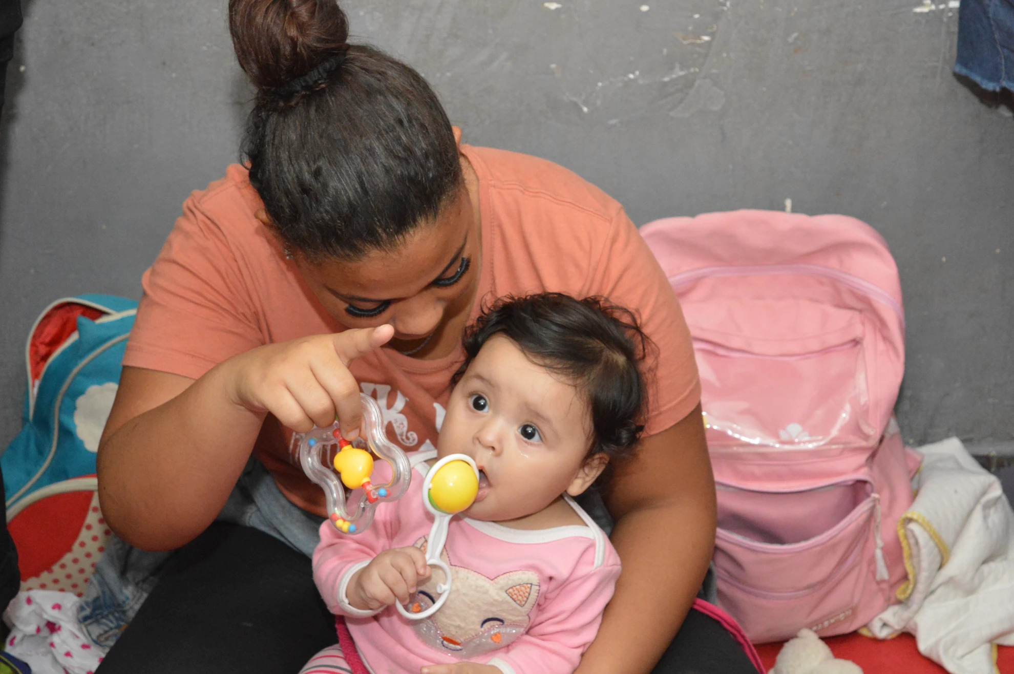 Mulher segurando bebê no colo com carinho e segurando brinquedos.