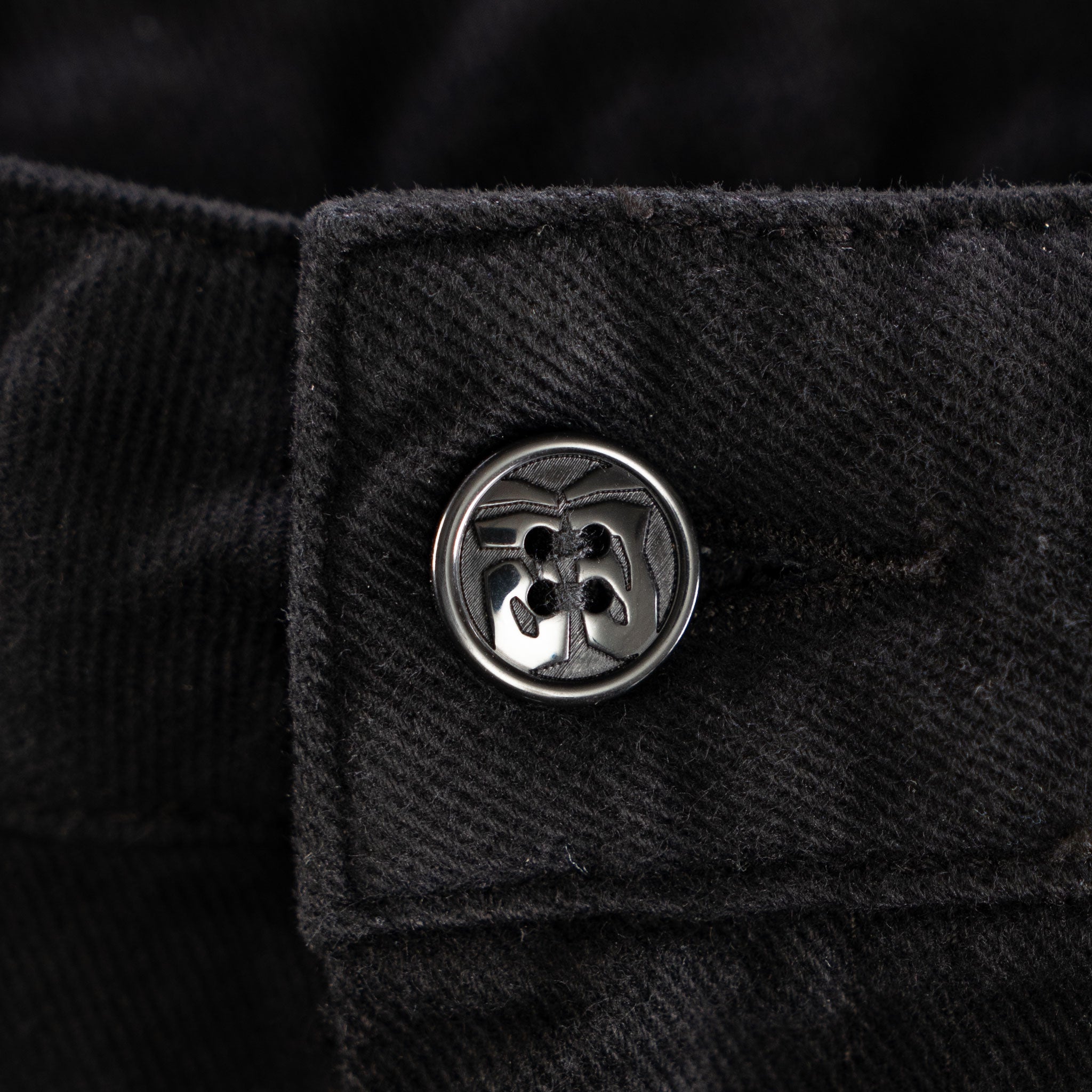 Close-up of a black textured fabric with a silver button featuring a floral design.