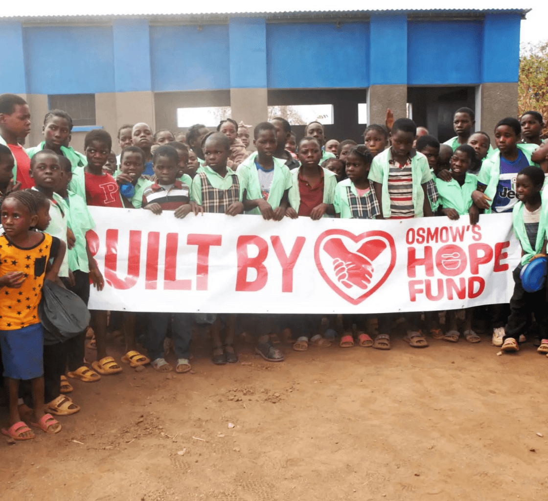 Osmow's Hope Fund built by community sign with group of local children gathered outside