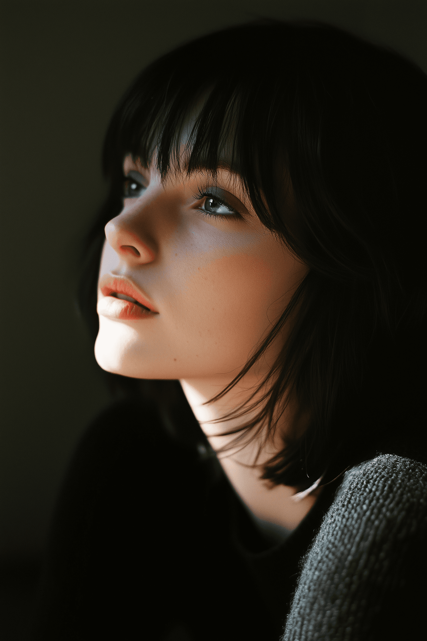Thoughtful young woman with dark hair and blue eyes gazes into the distance, illuminated by soft lighting.