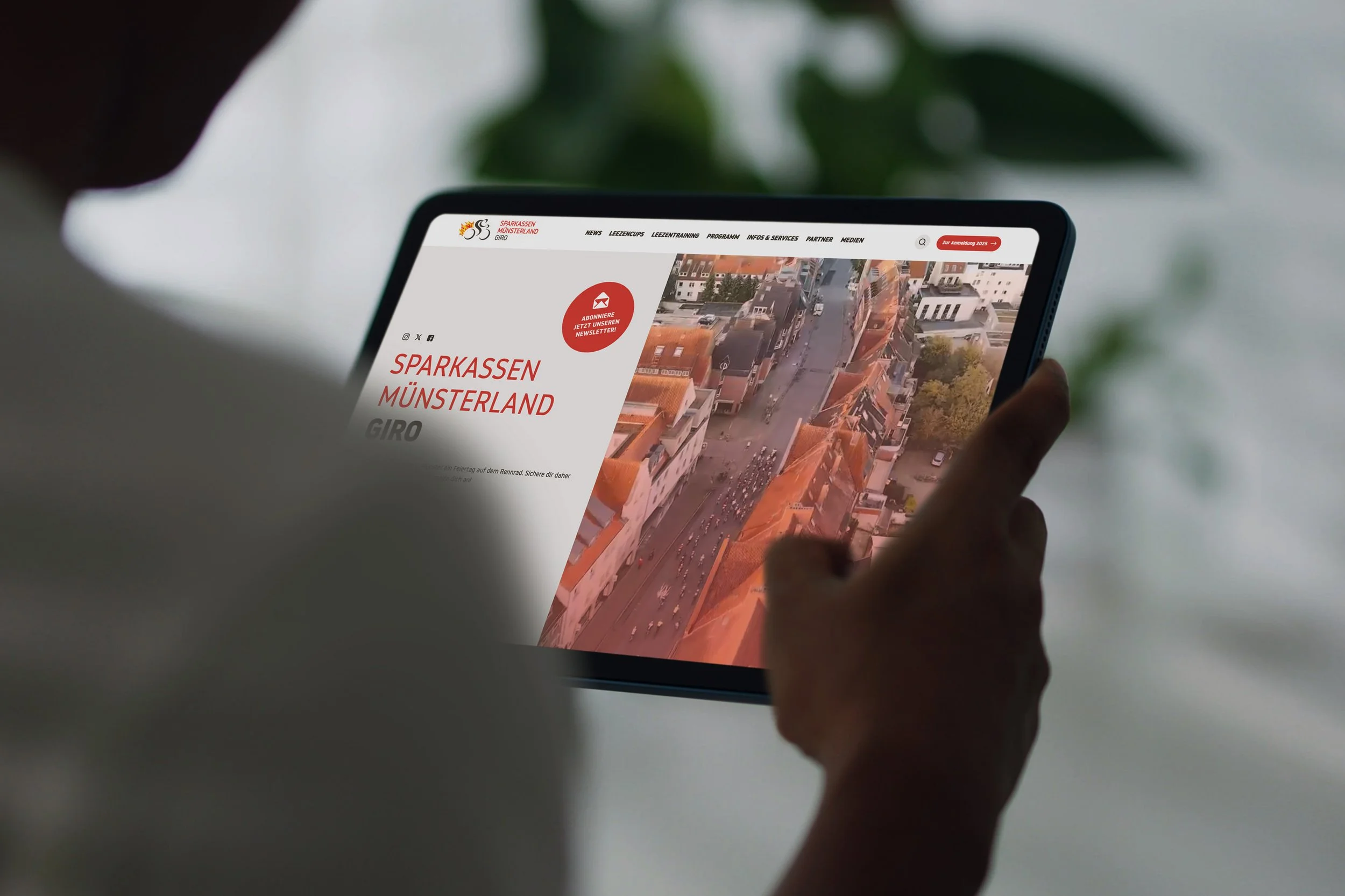 In einer Over-the-Shoulder-Aufnahme wird die Website des Sparkassen Münsterland Giro auf einem Tablet dargestellt. Die Website ist aus der Perspektive der nutzenden Person sichtbar und zeigt ein modernes, übersichtliches Webdesign.