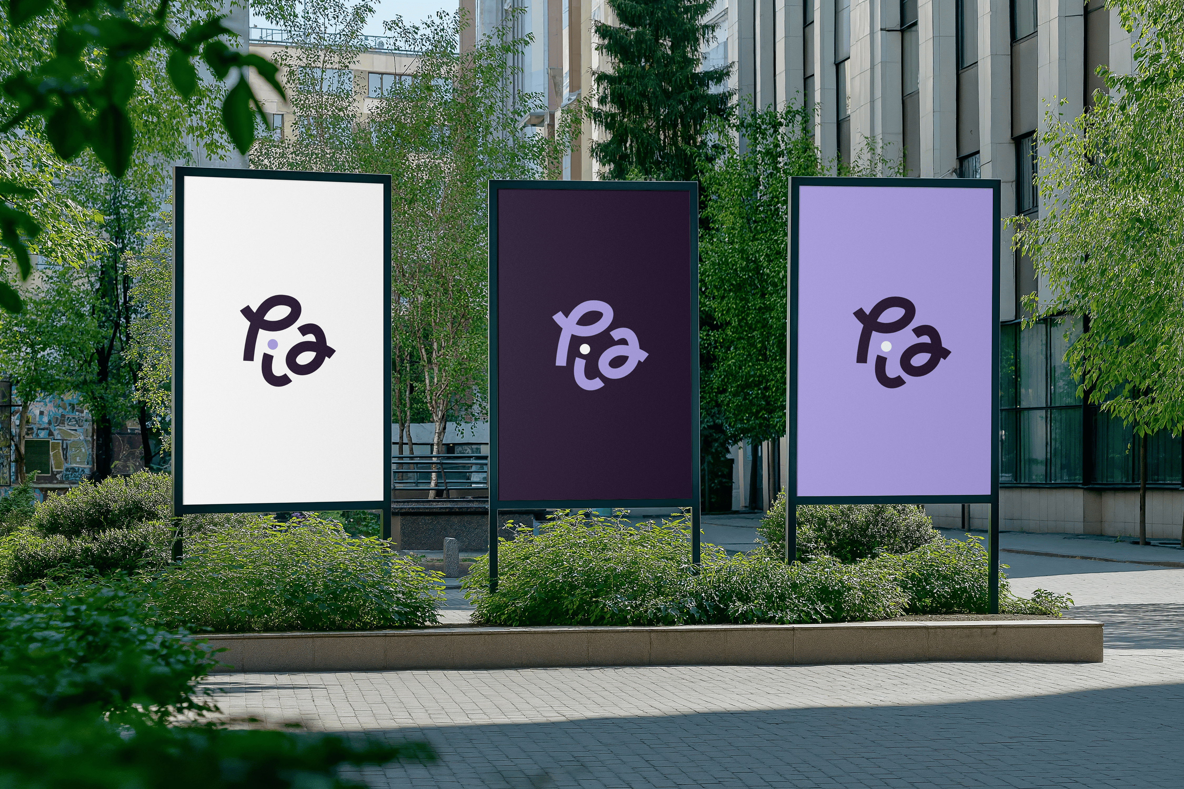 Three large outdoor billboards display the word "Pia" in a stylized font with varying backgrounds—white, dark purple, and lavender—set against a backdrop of modern buildings and lush greenery.