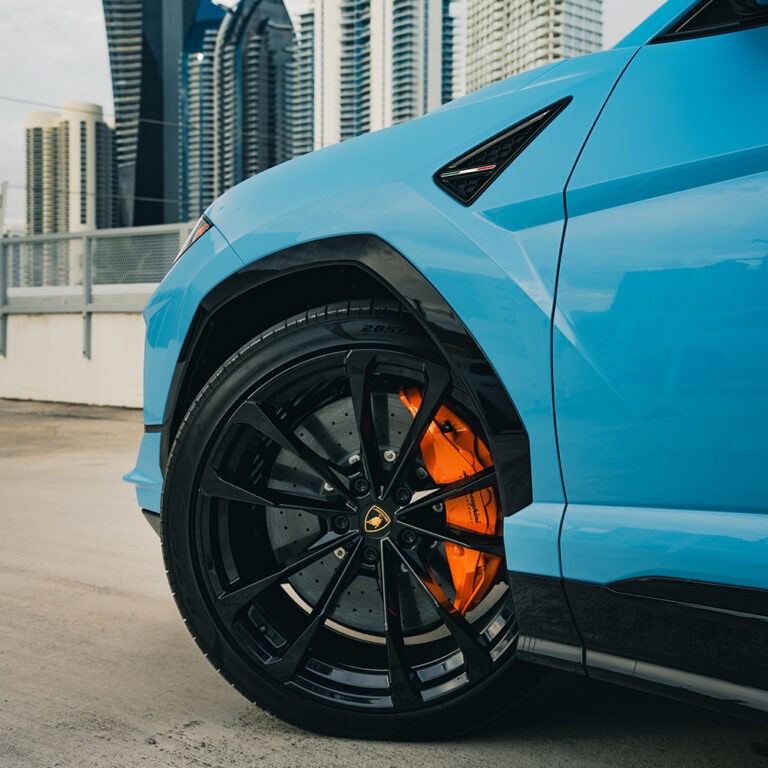 Close-up of blue Lamborghini Urus S wheel and orange brake caliper, performance details.