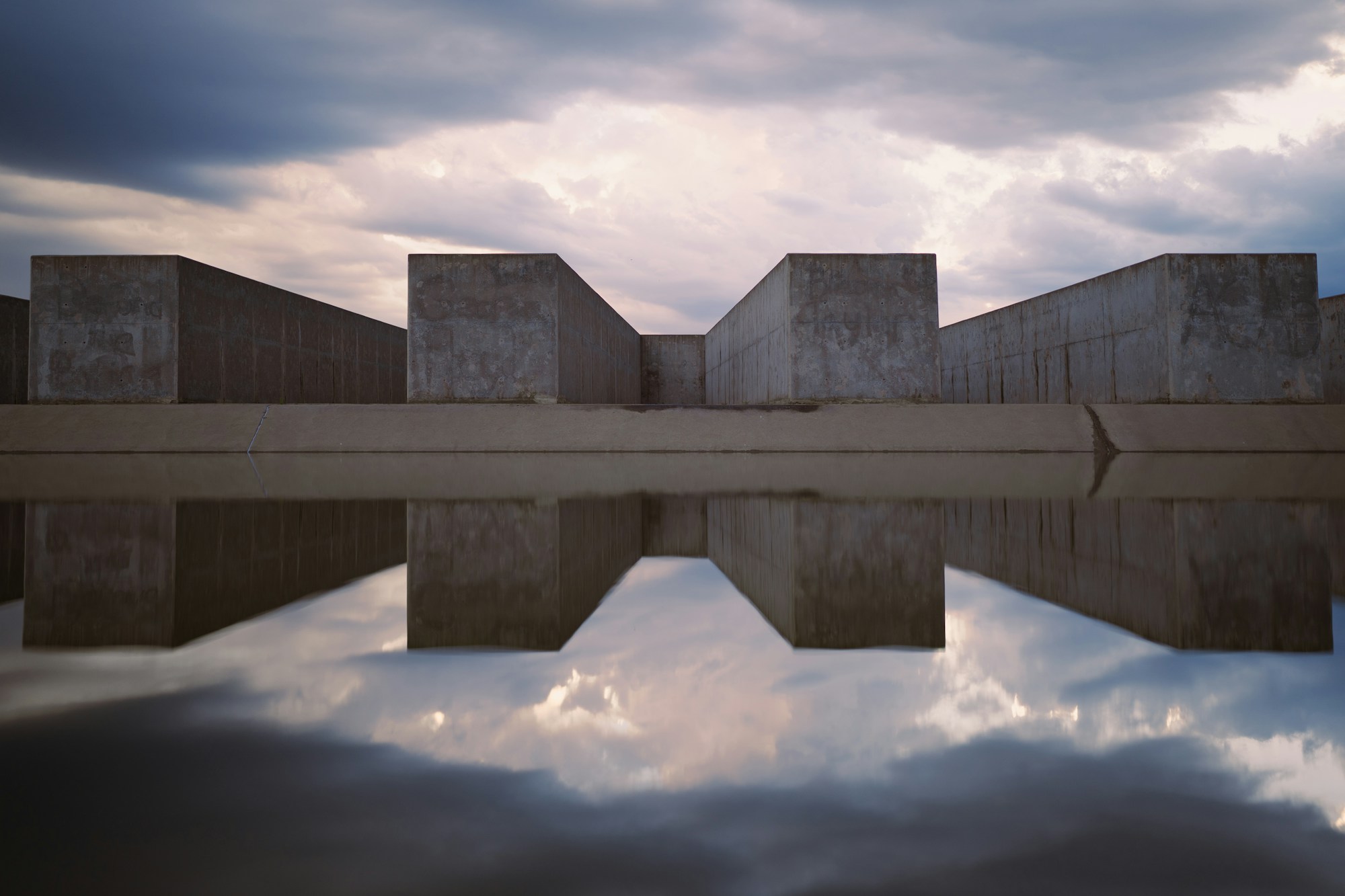 Concrete foundry bunkers mirrored in the old quench pond under a heavy sky