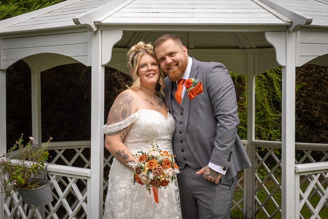Hannah and Shawn standing together under a garden gazebo at the Charlecote Pheasant Hotel