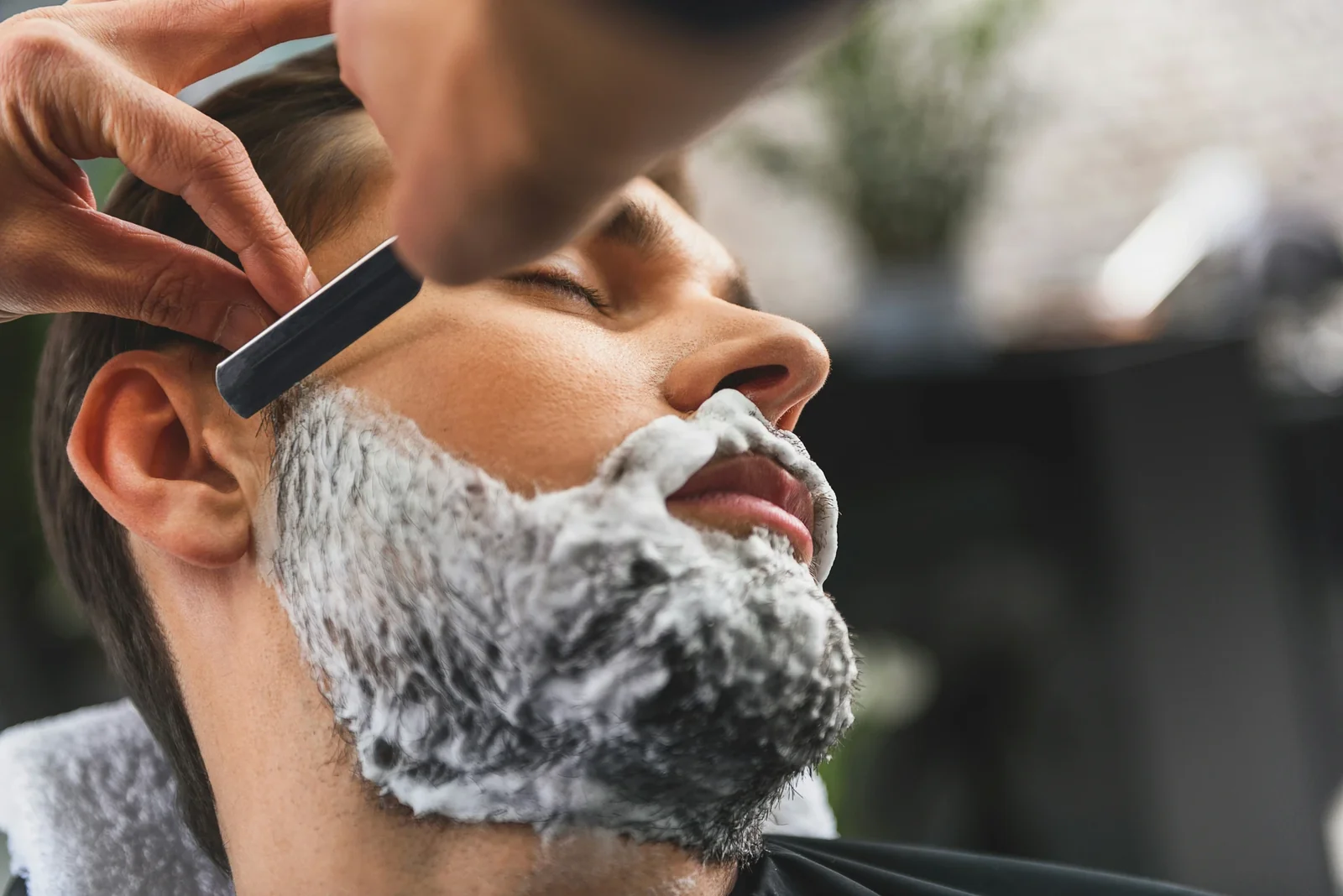 Barber applying shaving cream to client's face with razor during grooming service.