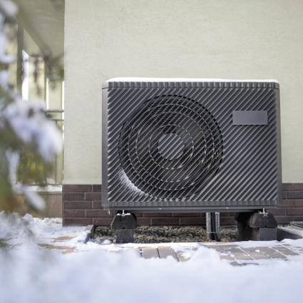 Air source heat pump outdoor unit on the side of a UK home discharging cold air normally during winter heating operation with frost visible on the coil