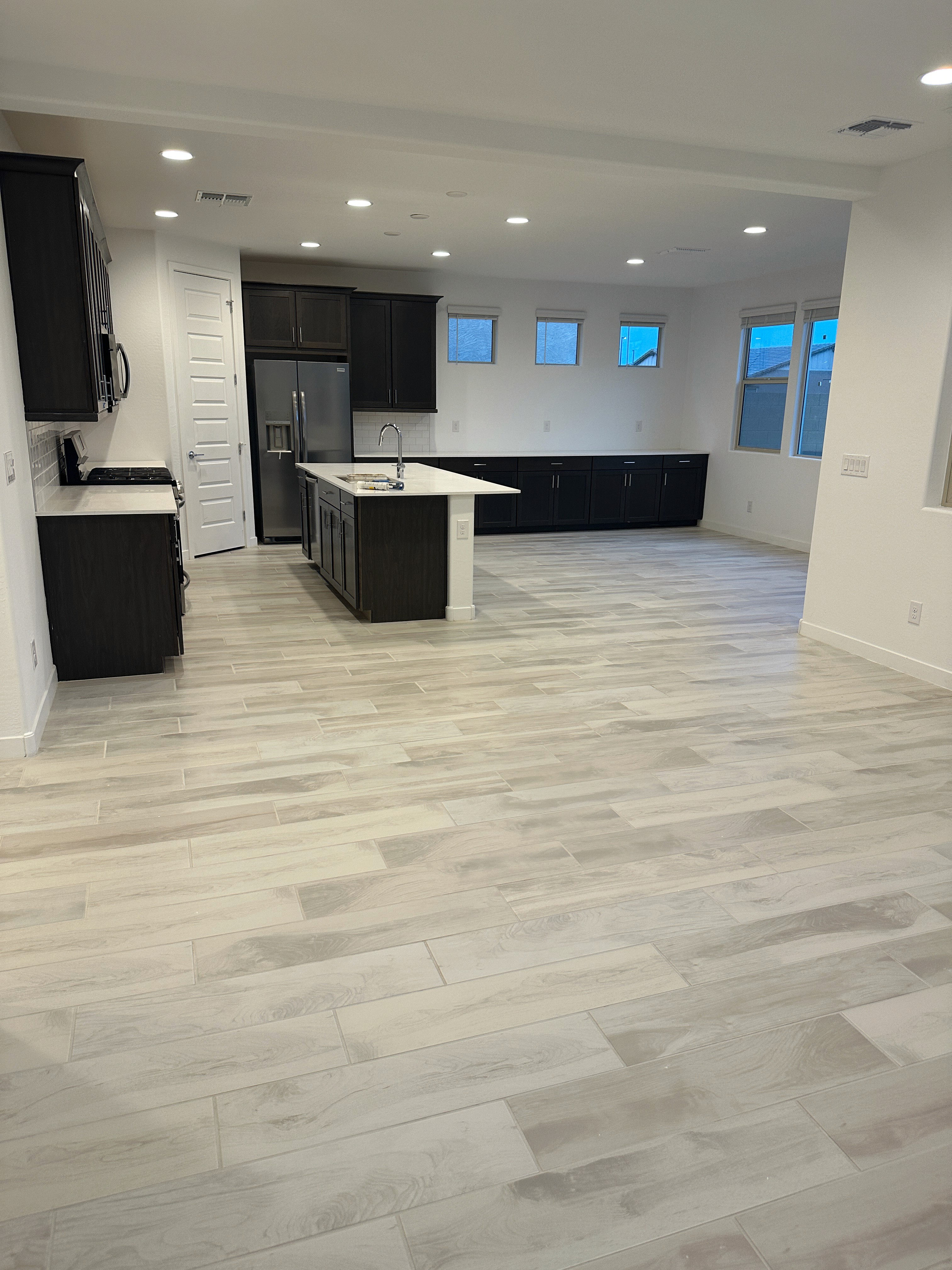 Modern kitchen with dark cabinets, white island, and wood-look tile flooring in an open-plan living area during construction.