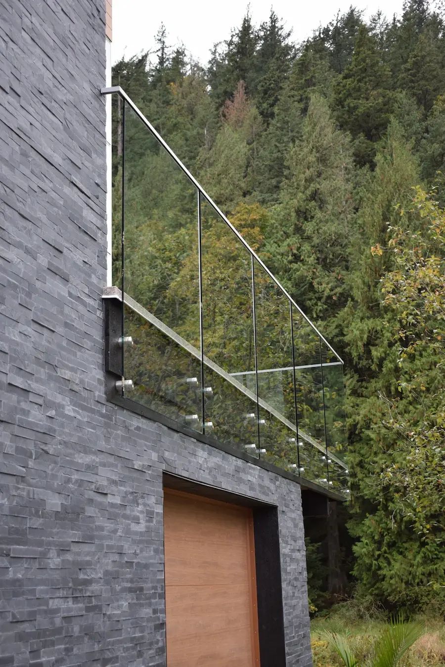 Condo balcony glass railings for Vancouver featuring clear glass panels mounted within a steel frame, installed on an upper-level balcony overlooking a forested residential setting.