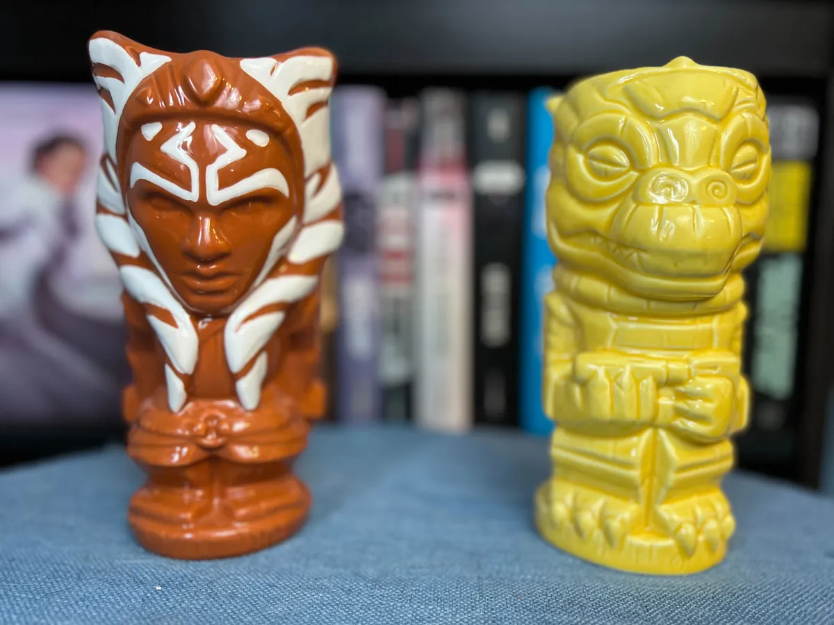 Geeki Tiki mugs with Ahsoka Tano and Bossk designs on a blue surface in front of a blurred Star Wars bookshelf