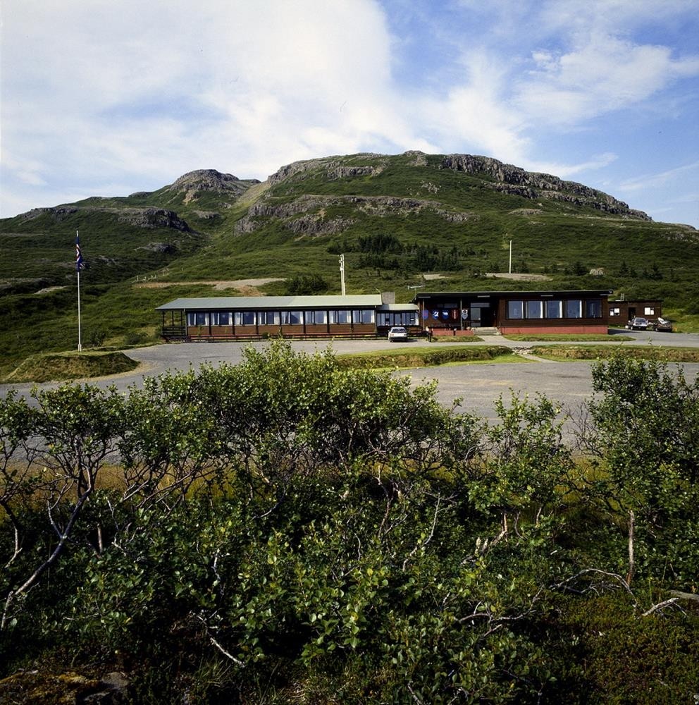 Hótel Flókalundur on a sunny summer day, with birch scrub in the foreground and the mountain behind