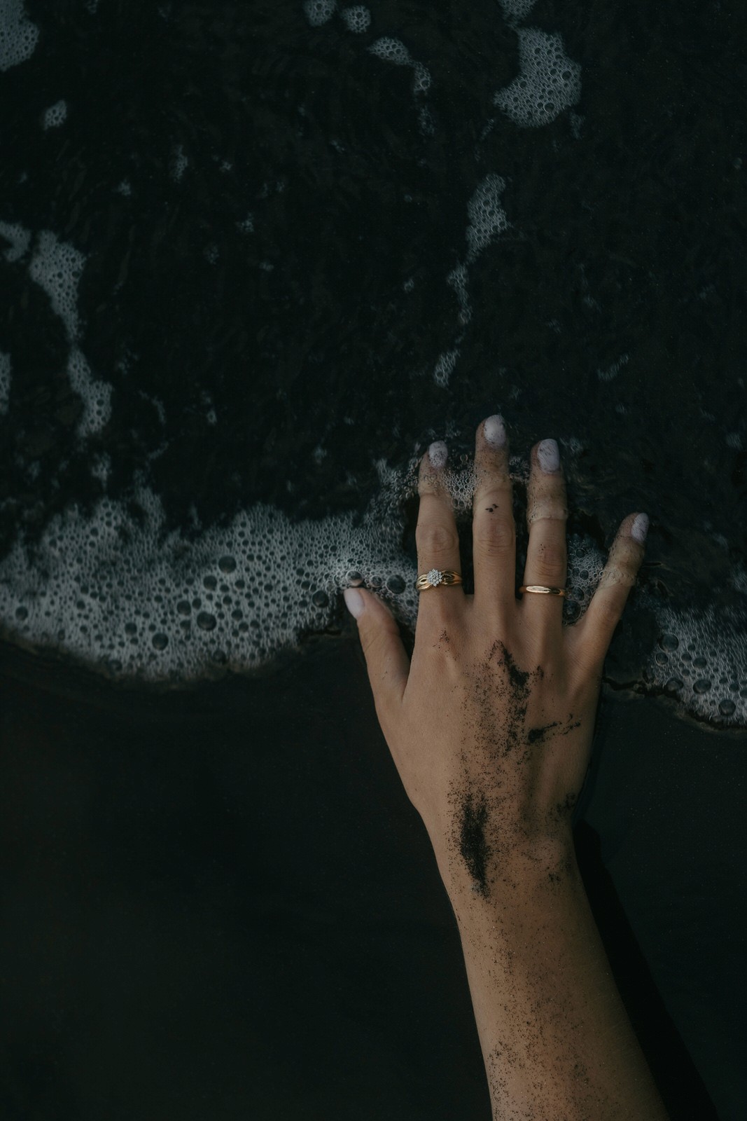hand with wedding ring touching the black volcanic beach at Seixal
