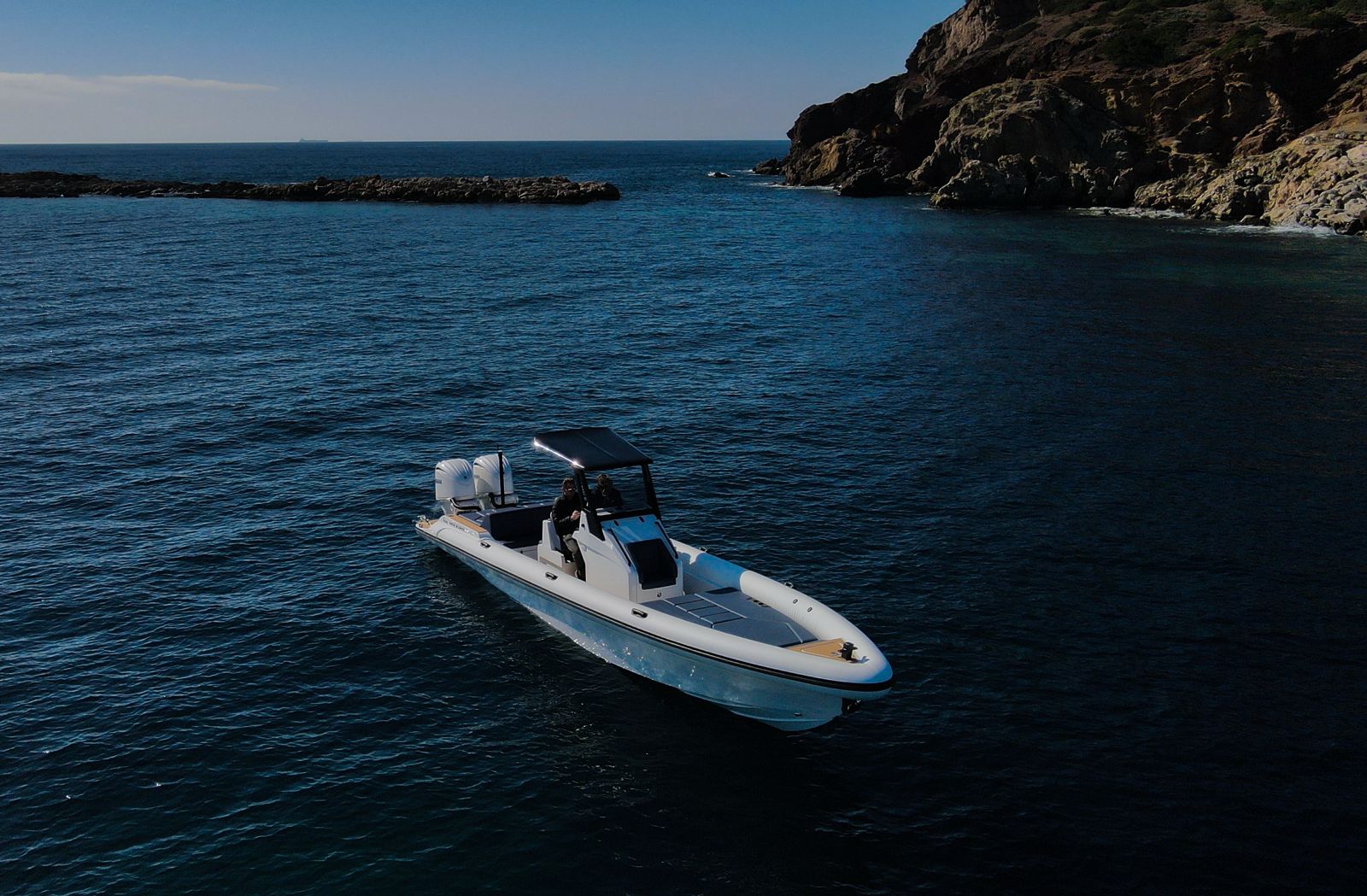White Rock 36 speedboat with captain at helm cruising calm blue waters near Paros coastline with hills in background.