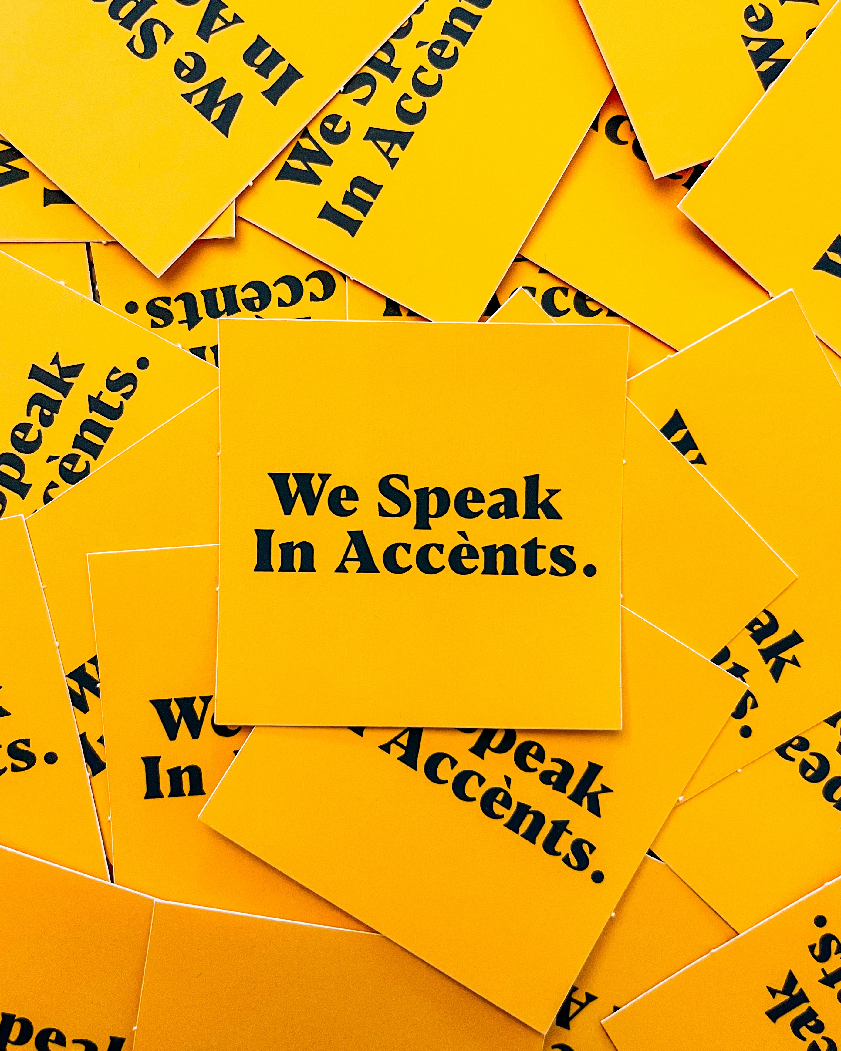 A bunch of yellow stickers that read 'we speak in accents'
