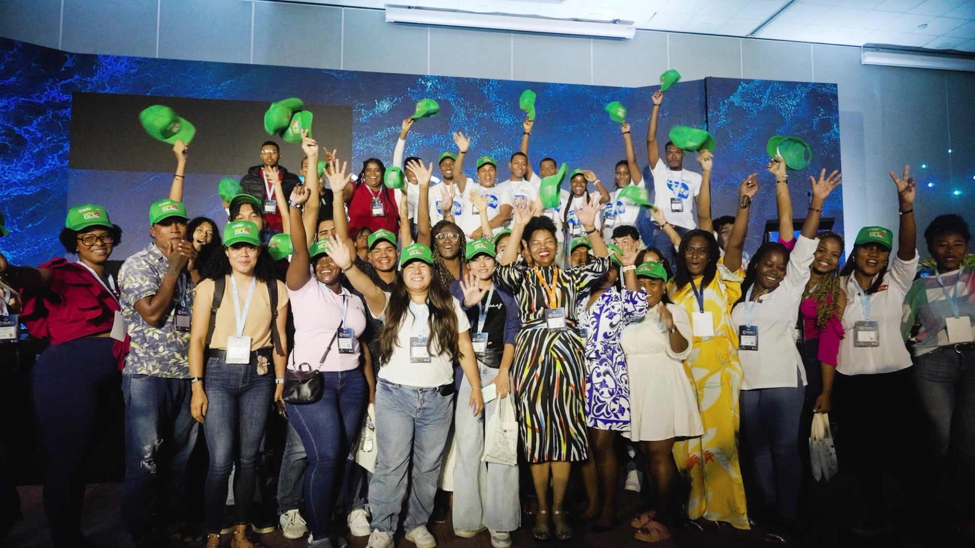 Grupo de participantes con sombreros verdes celebrando con los brazos en alto en el escenario del CILAC