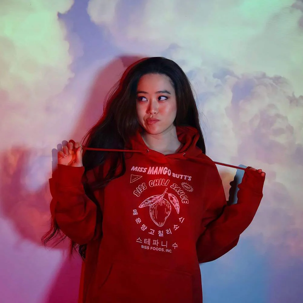 A person in a red hoodie stands against a colorful, cloud-like background, holding a string with both hands.