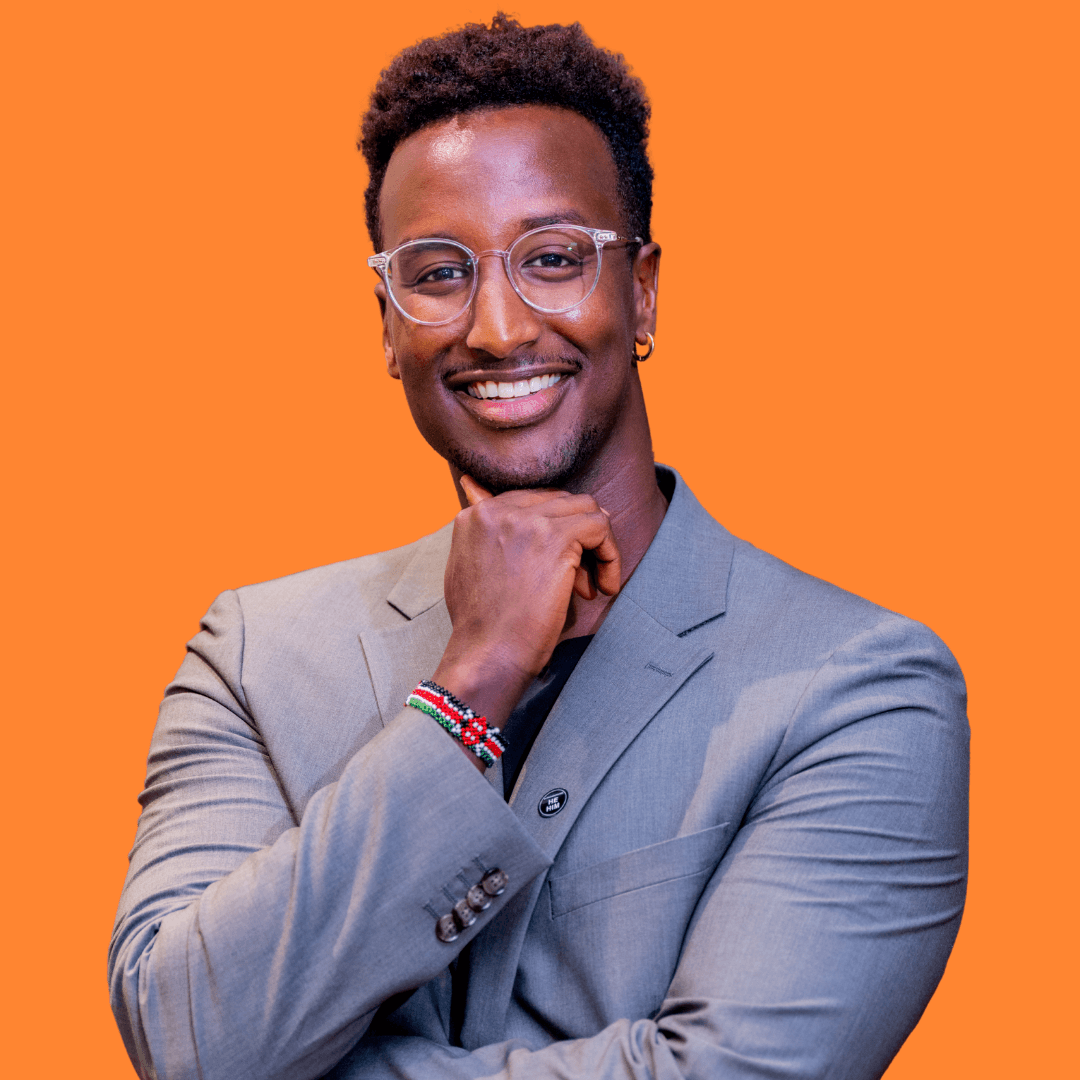 Smiling individual in a white shirt against an orange background, sitting with hands resting on knees.