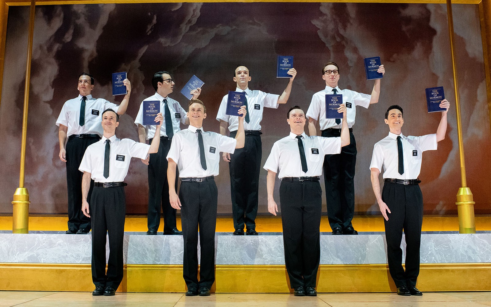 Performers holding books on stage in "The Book of Mormon" musical.