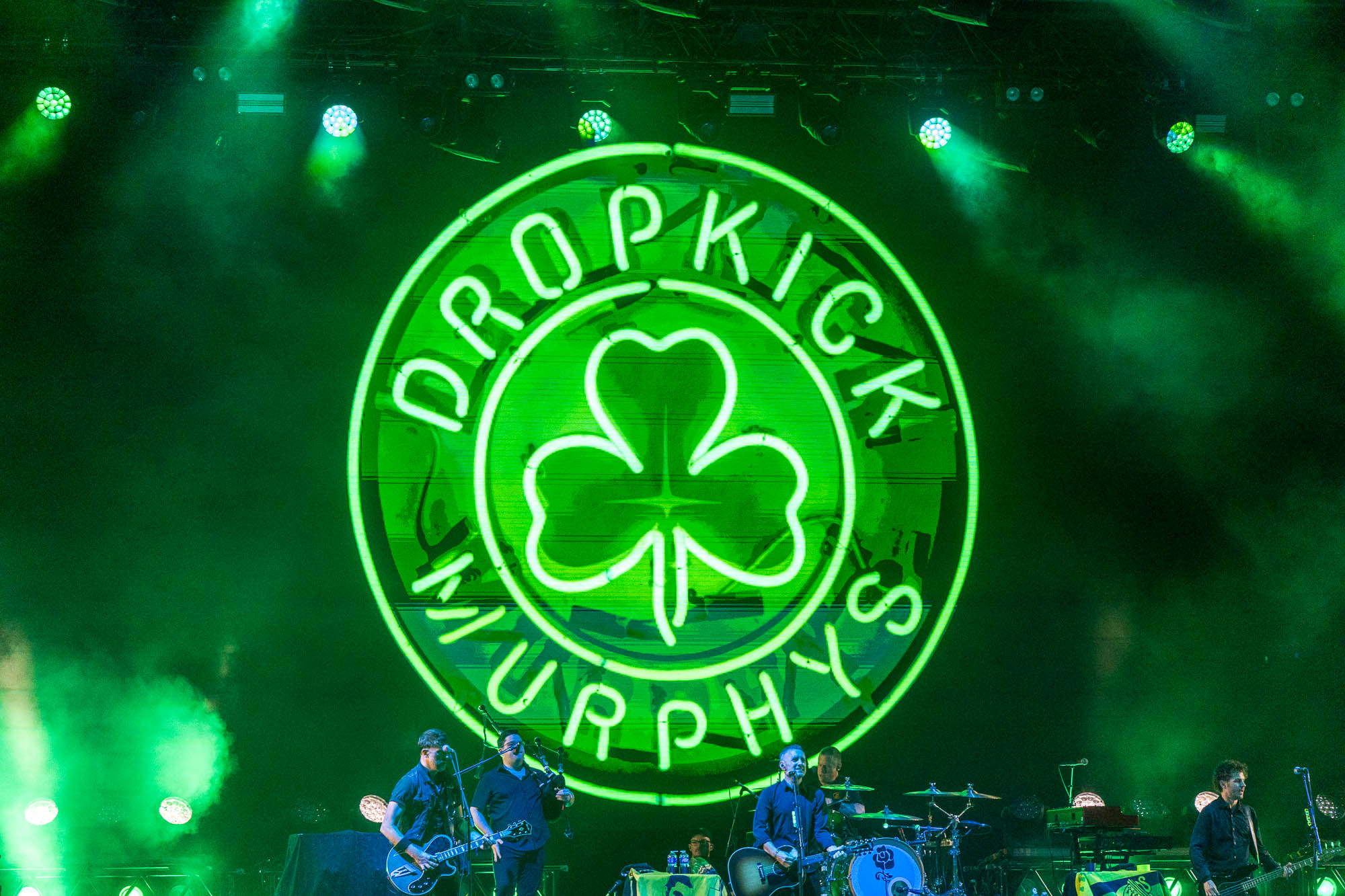 Logo néon vert des Dropkick Murphys au-dessus des musiciens sur scène.