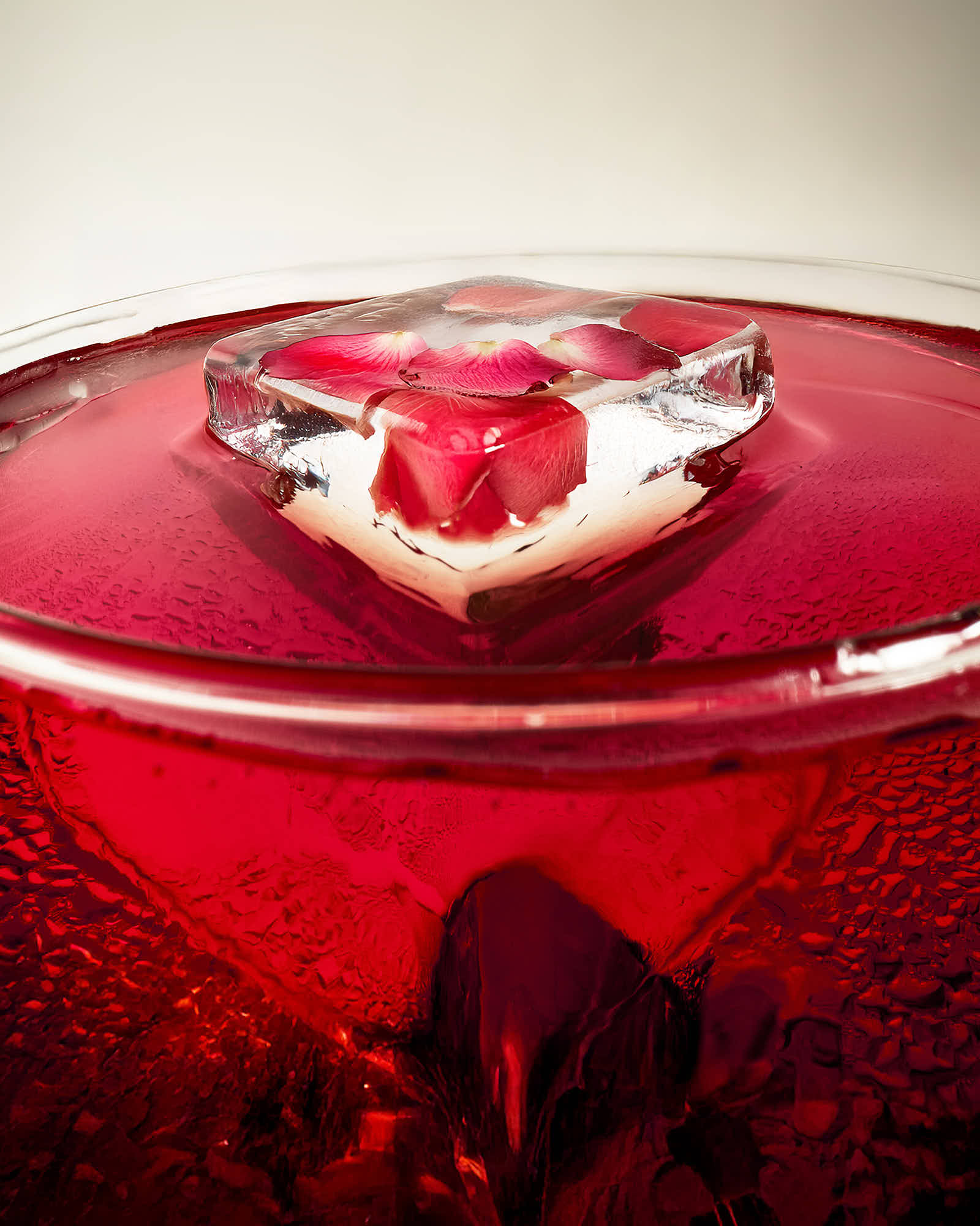 A close-up of a red drink topped with a shiny cherry, set against a light background.