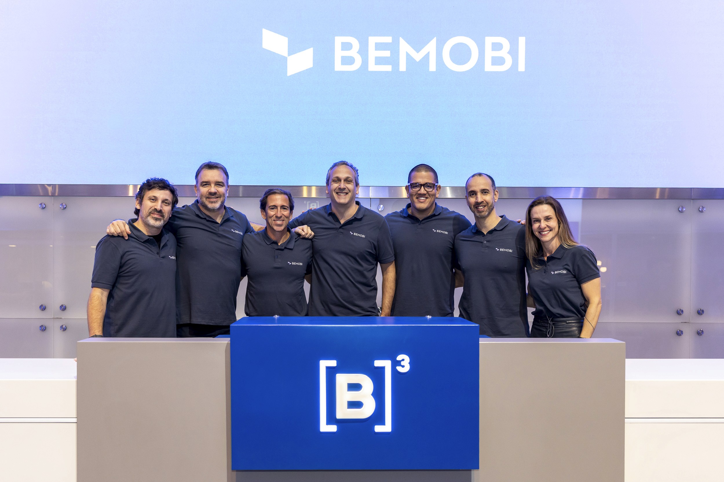 Bemobi executives behind the B3 podium at the bell ringing for 5 years of BMOB3, with the Bemobi brand on the screen