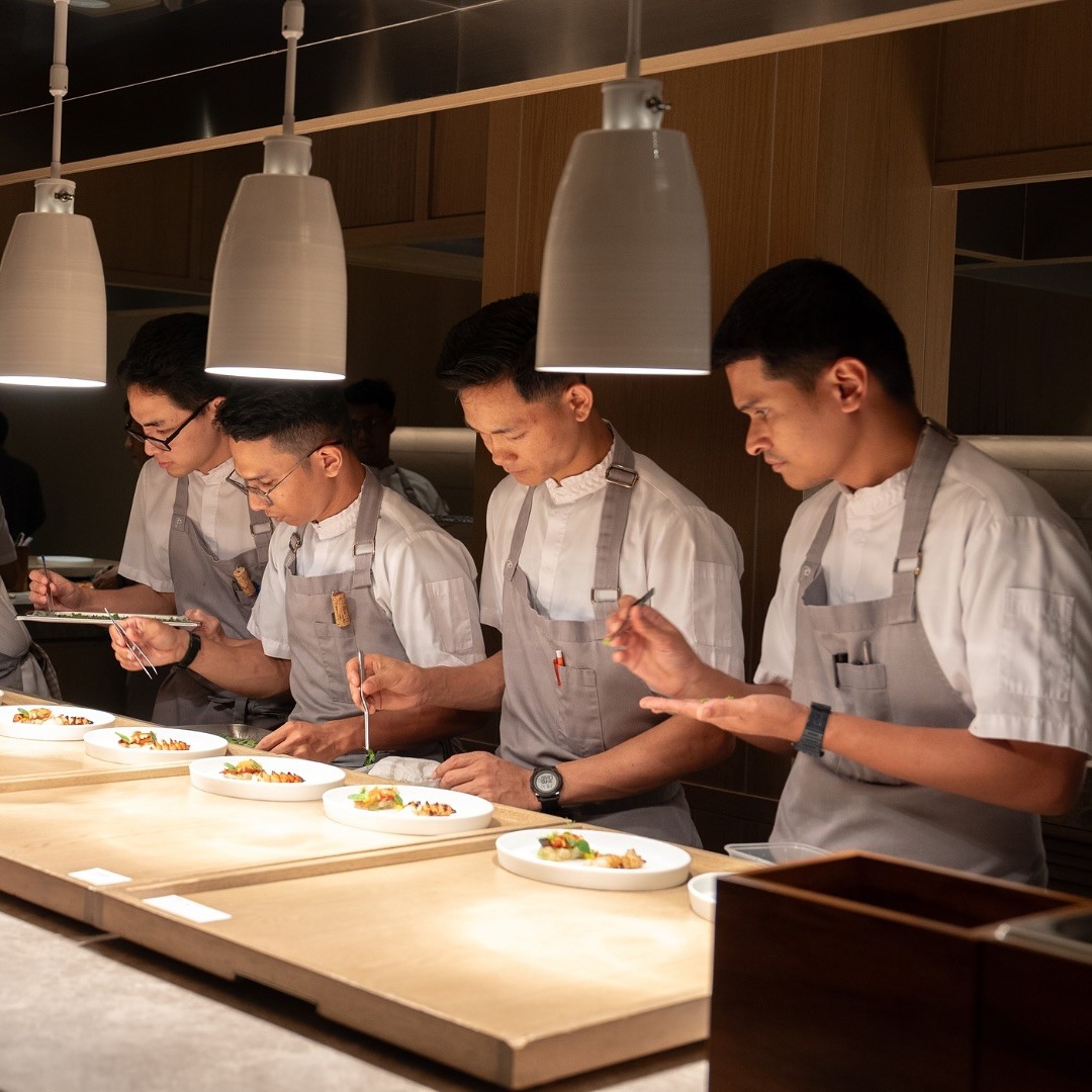 Four chefs meticulously plating dishes in a modern kitchen setting at Potager restaurant, showcasing a fine dining experience.