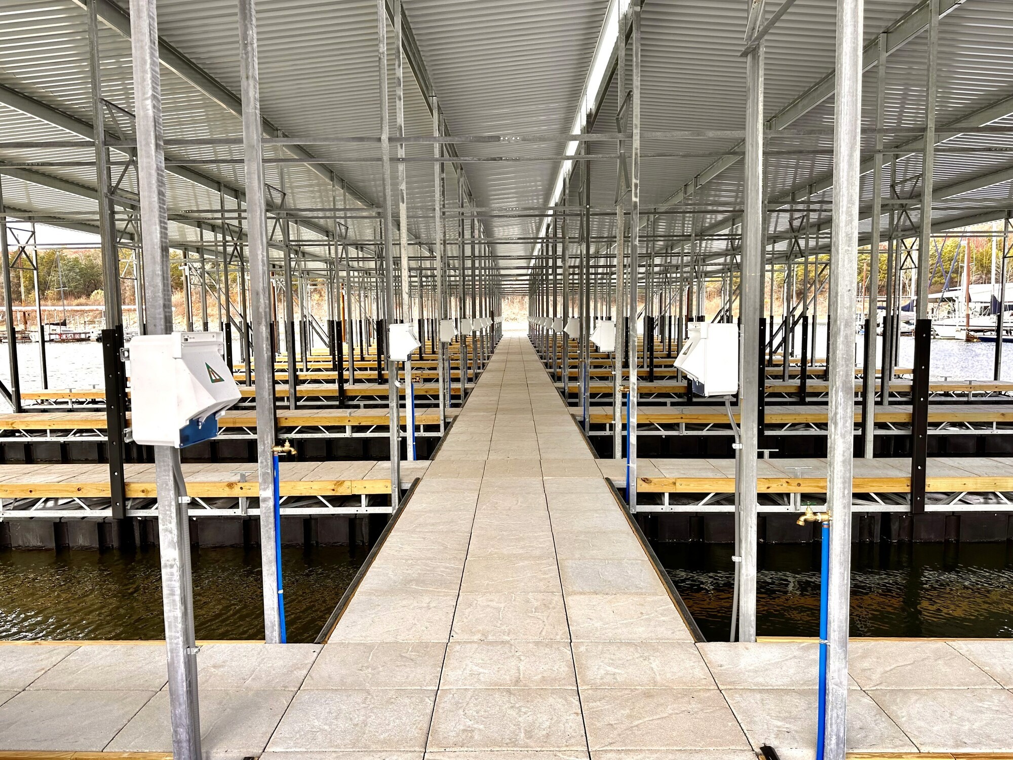 A covered boat dock structure stretches into the distance with multiple empty slips, surrounded by calm water and supported by metal framework, illustrating an organized, marina environment.