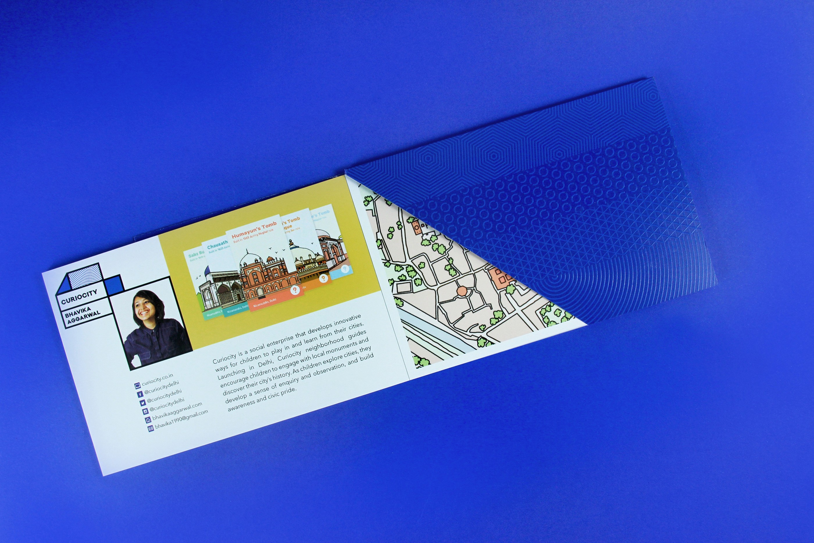 A blue envelope with an opened notebook coming from it. On the notebook there is a picture of a woman, some drawings of buildings, a text and a map of a city.