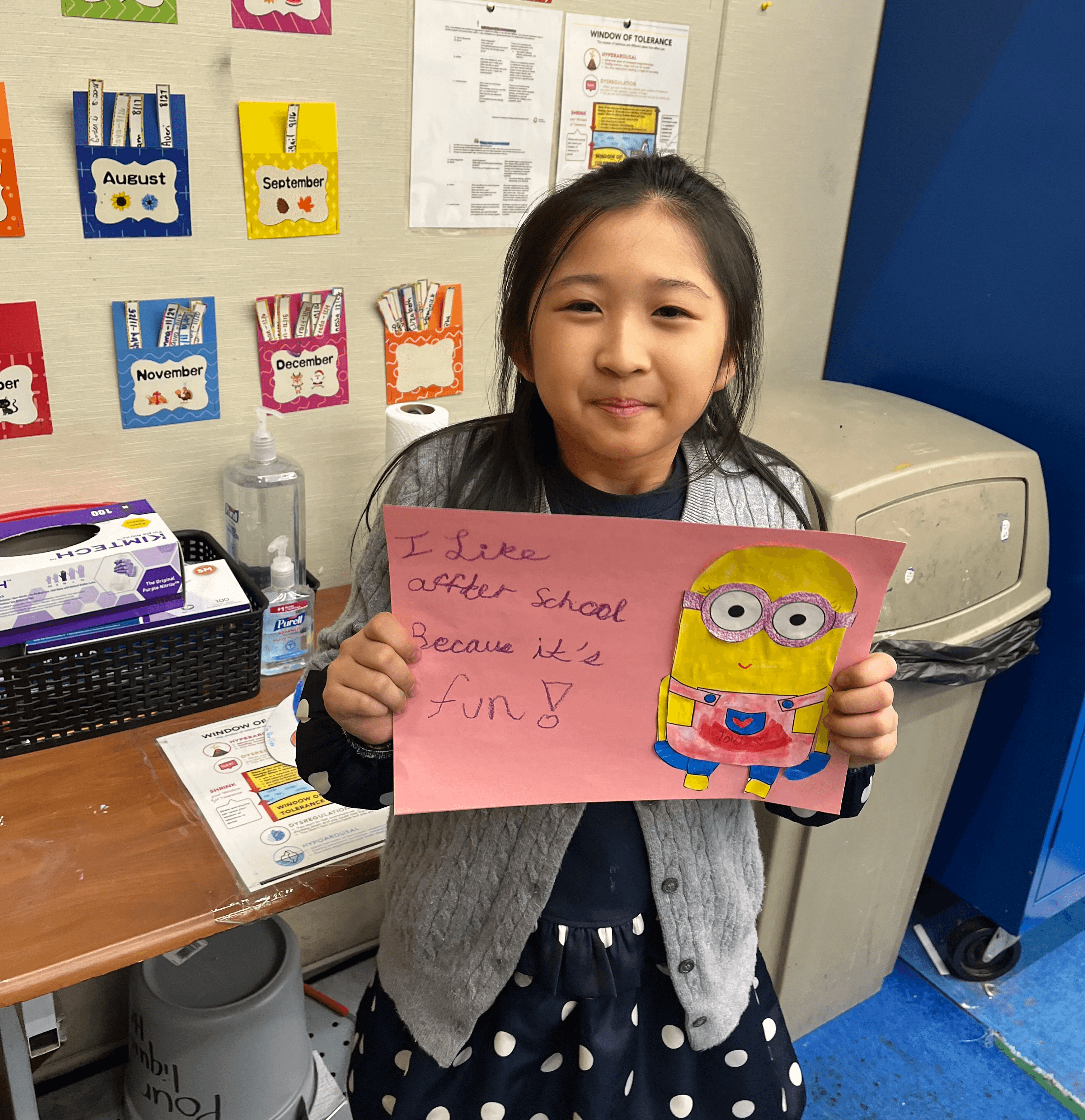 A young participant displays her Minion drawing, with cursive writing that reads "I like afterschool because it's fun!"