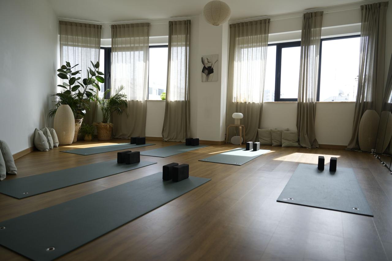 Close-up of yoga mats arranged with black support blocks in a sunlit studio room with soft beige curtains and a minimalist stool in the background.