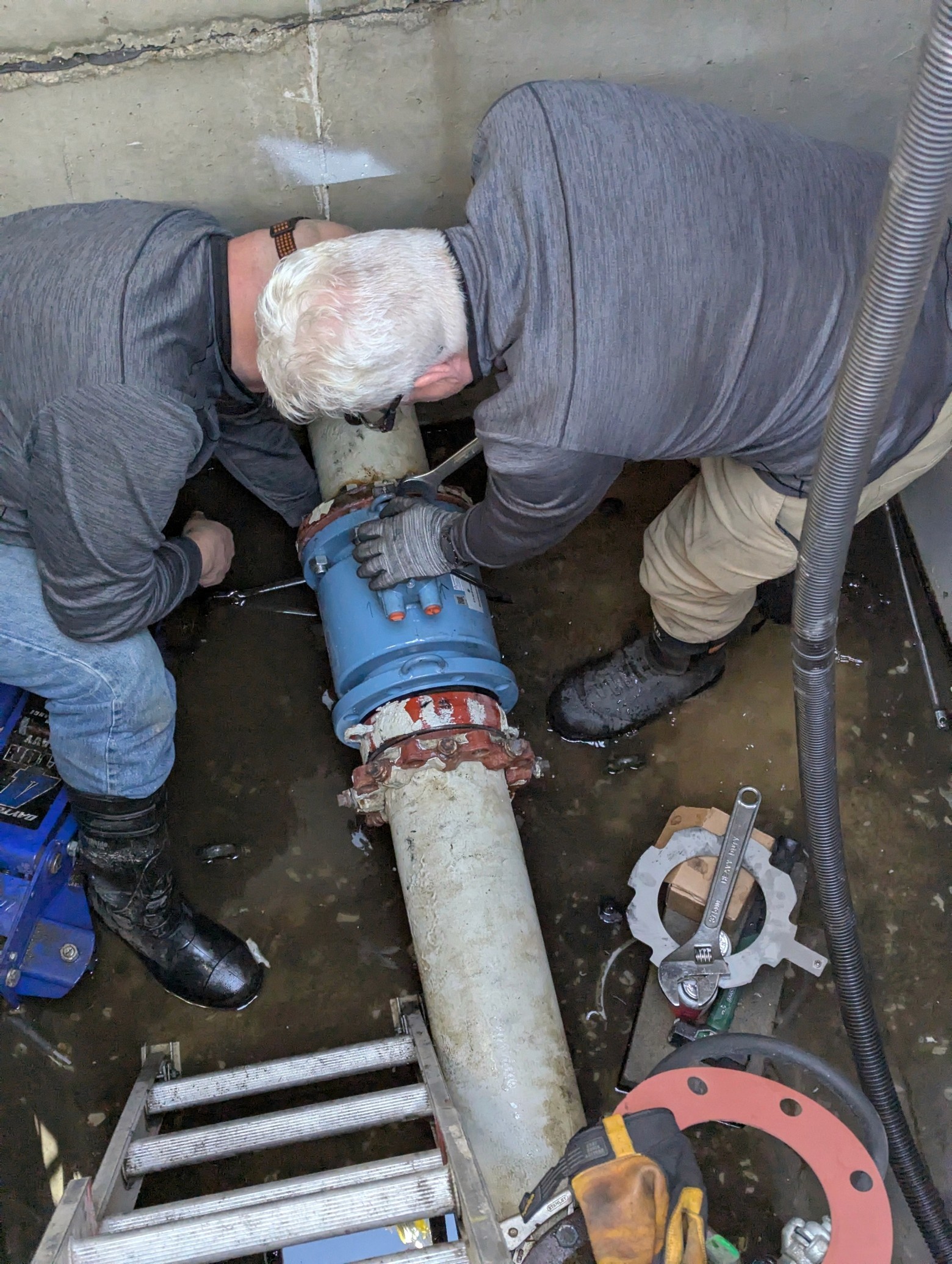 Two technicians aligning a blue flow meter on large piping inside a meter vault