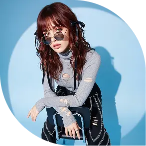 a model sitting with brown hair, black sunglass, bag in her hand and wearing a light gray t-shirt