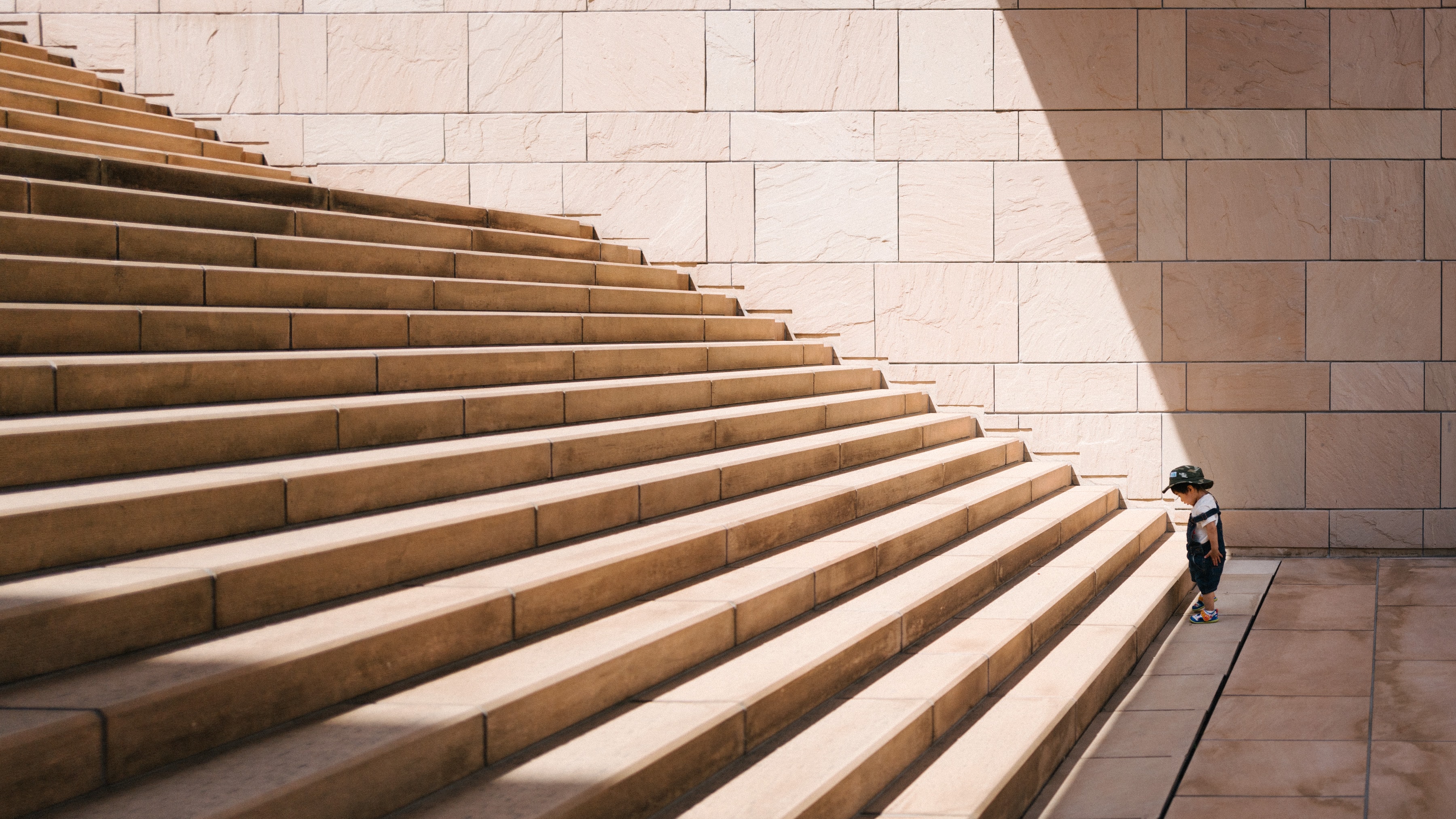 A boy in front of a very large set of stairs looking down.