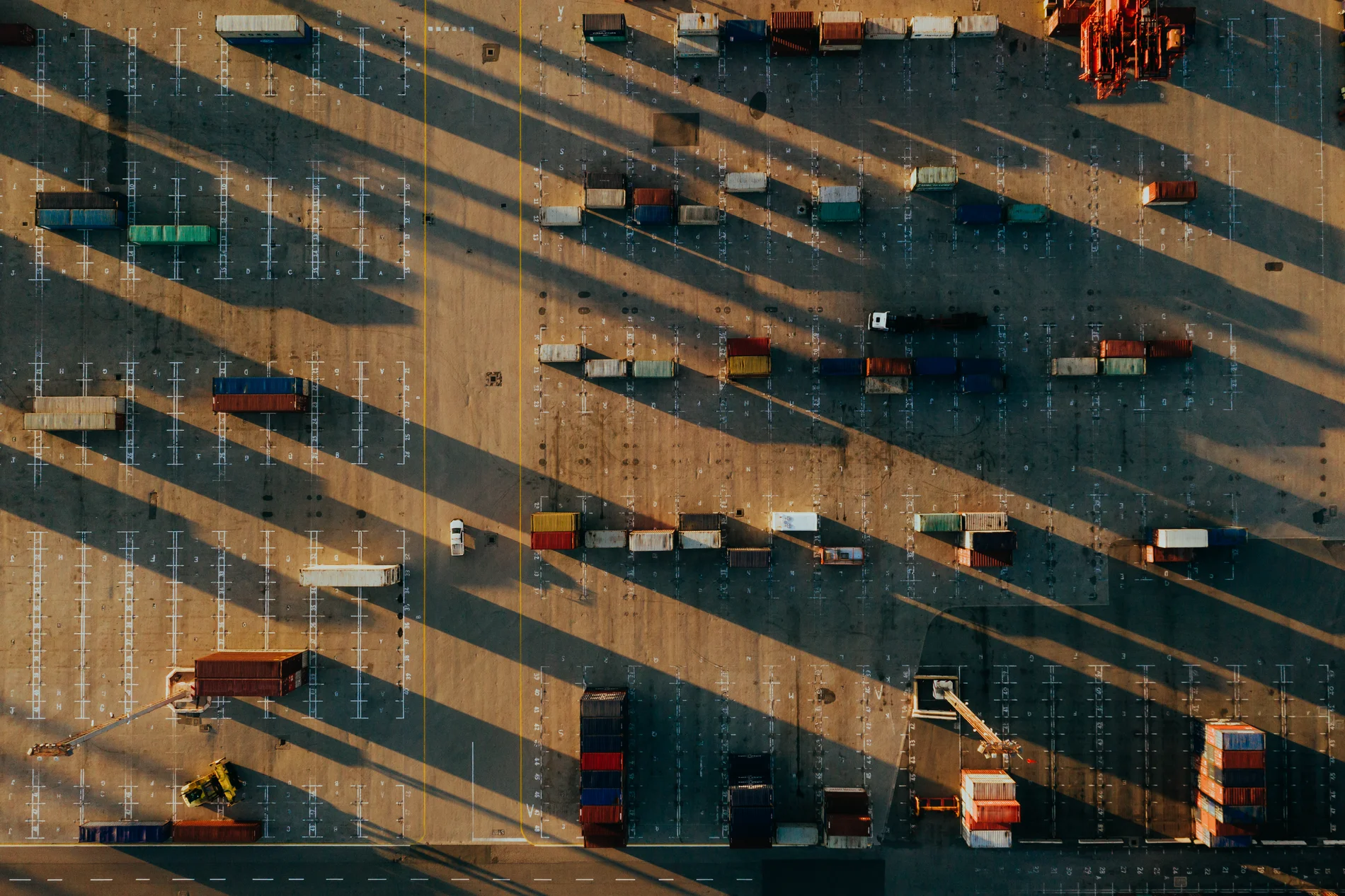 Aerial of a container yard at sunrise, containers and trucks throwing long parallel shadows