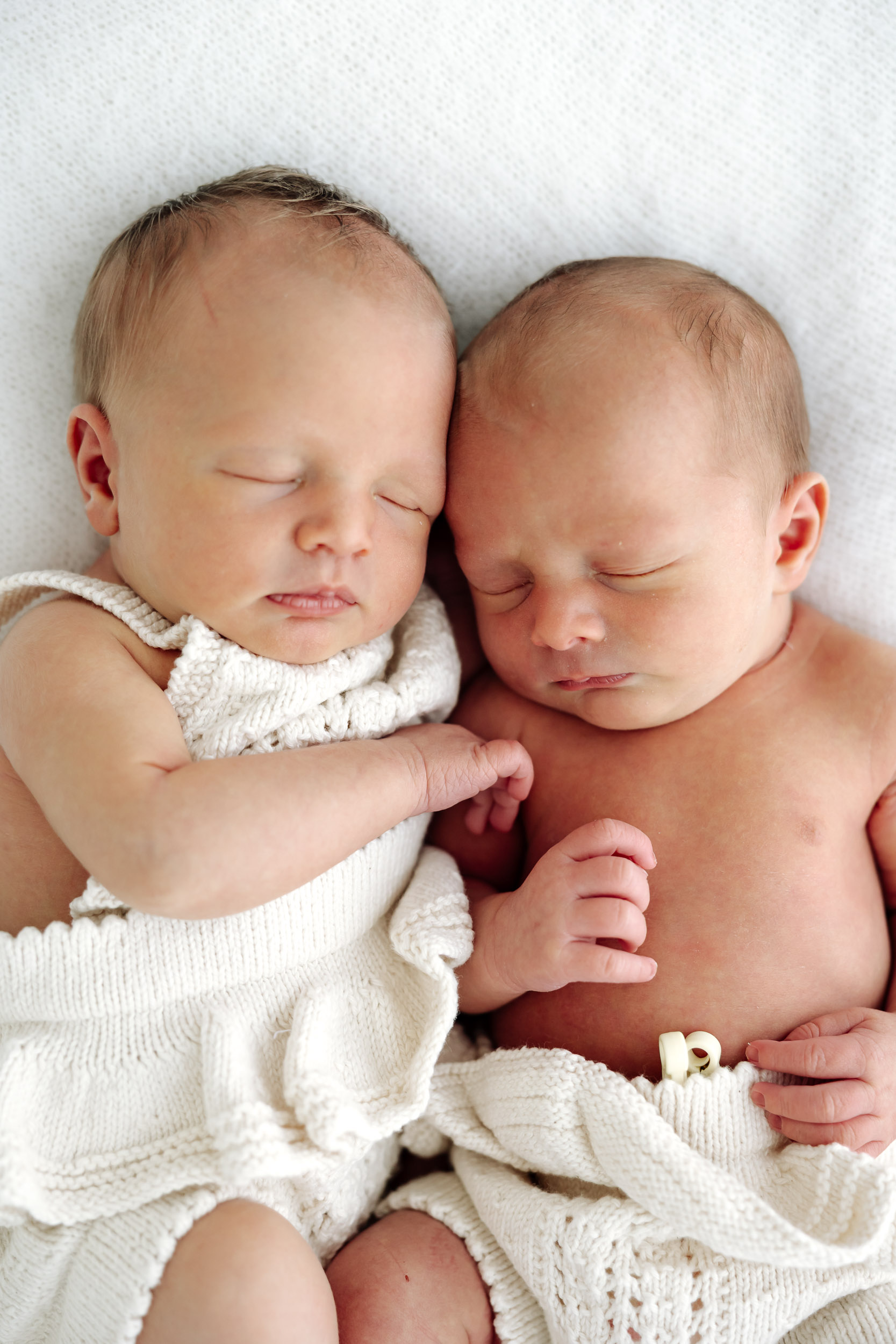 Professional twin newborn session in Mackay Queensland, identical babies cuddled side by side in soft white studio setting.