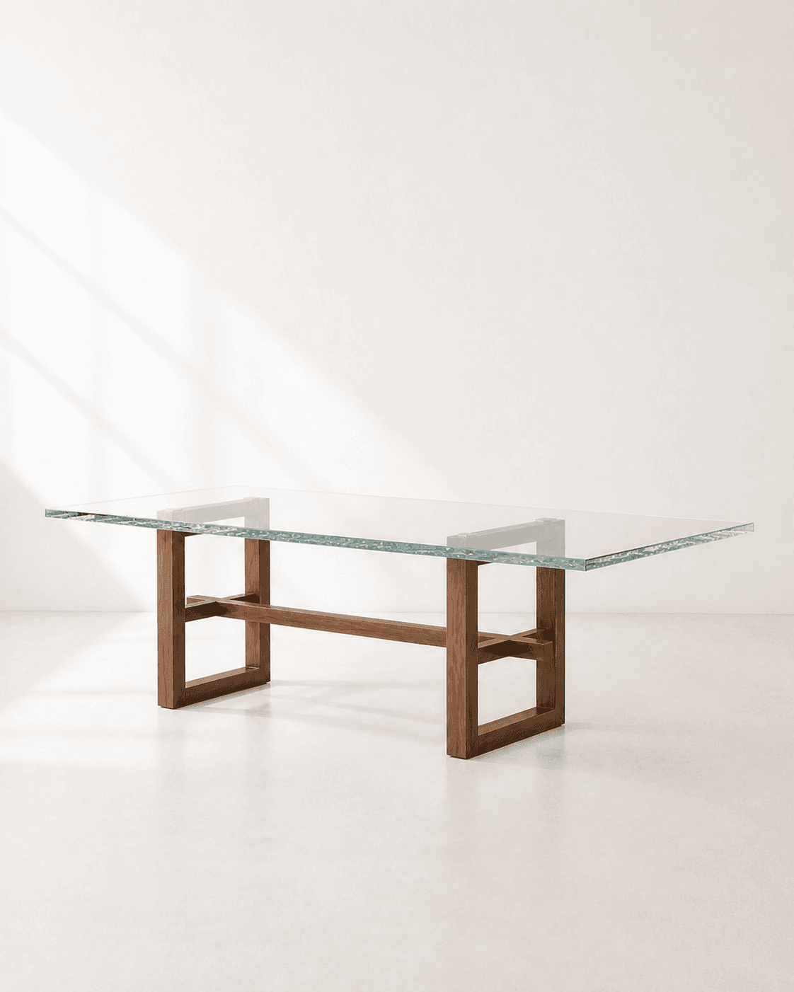 Alternative three-quarter view of Lumen Dining Table, showing a clear cast-glass top on intersecting walnut trestles