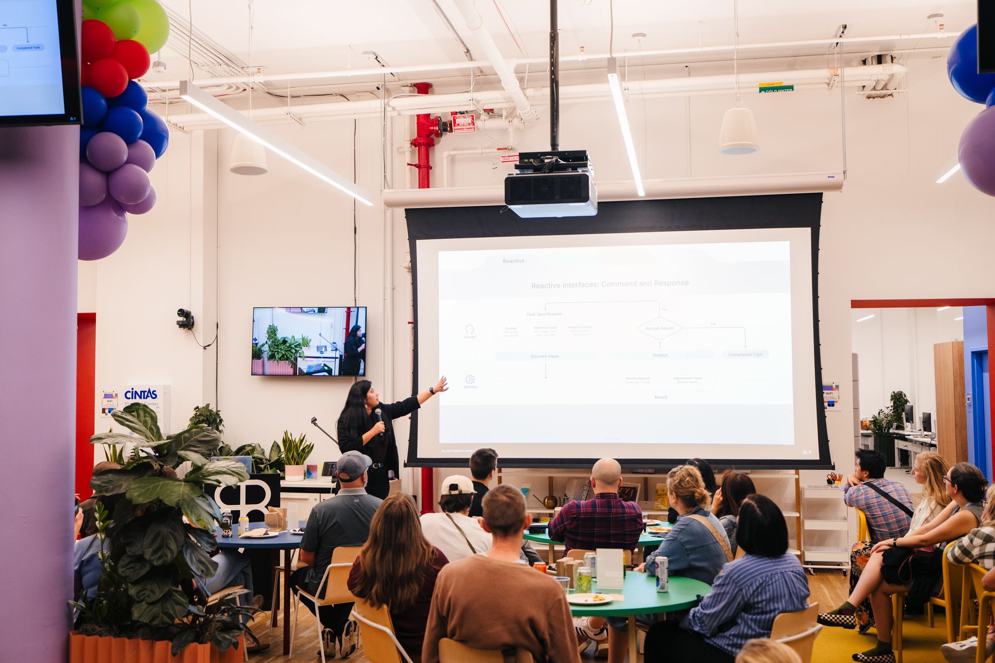 Gurusha Raskar speaking with a microphone at Figma x SmashingConference, above a wide shot of the room watching her present