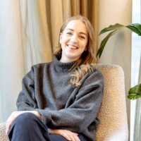 Smiling man with light brown hair and stubble, wearing a khaki shirt in natural light