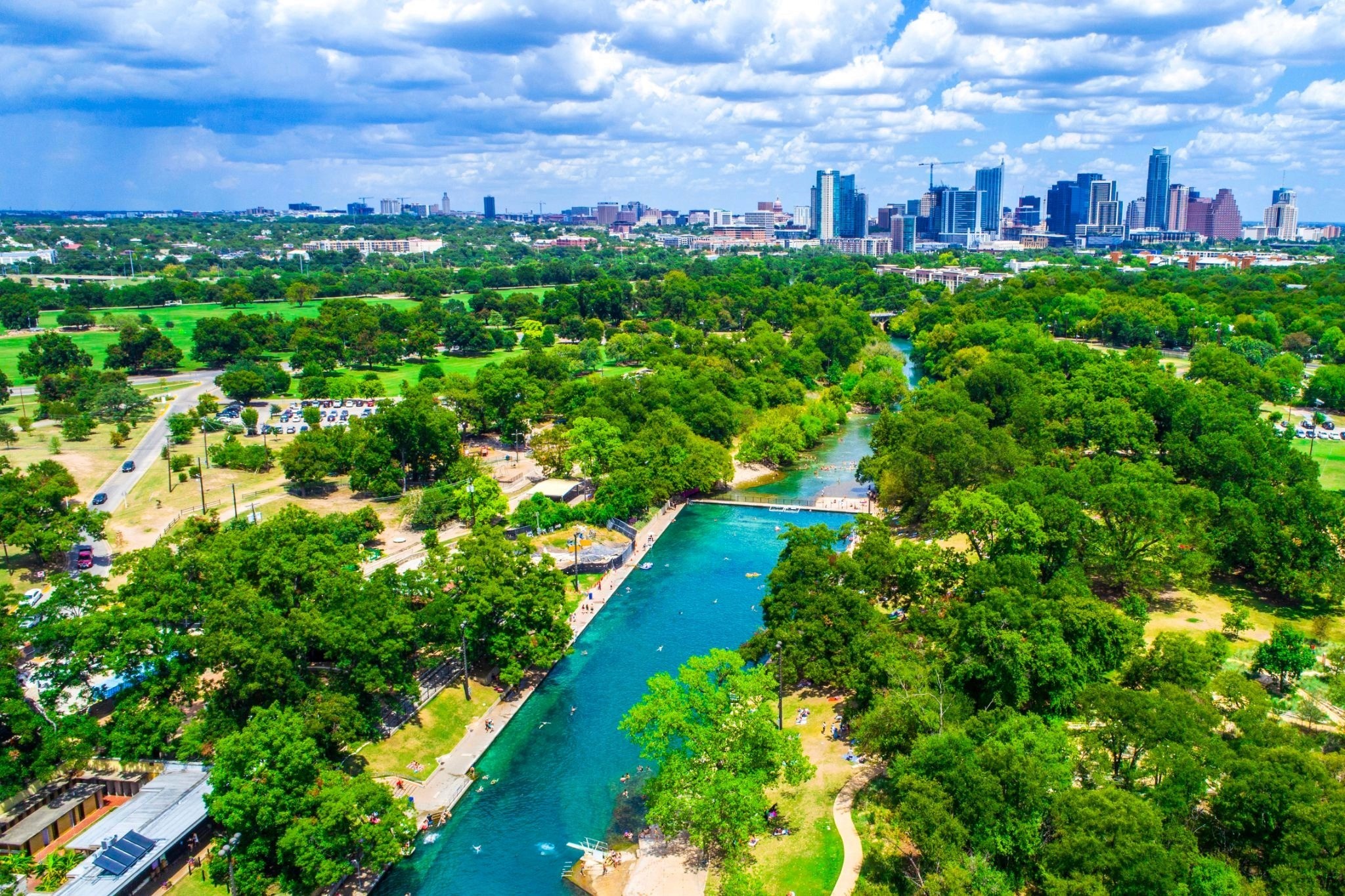 An aerial shot of leafy parkland with a river running through it, and the skyscrapers of Austin, Texas, in the background