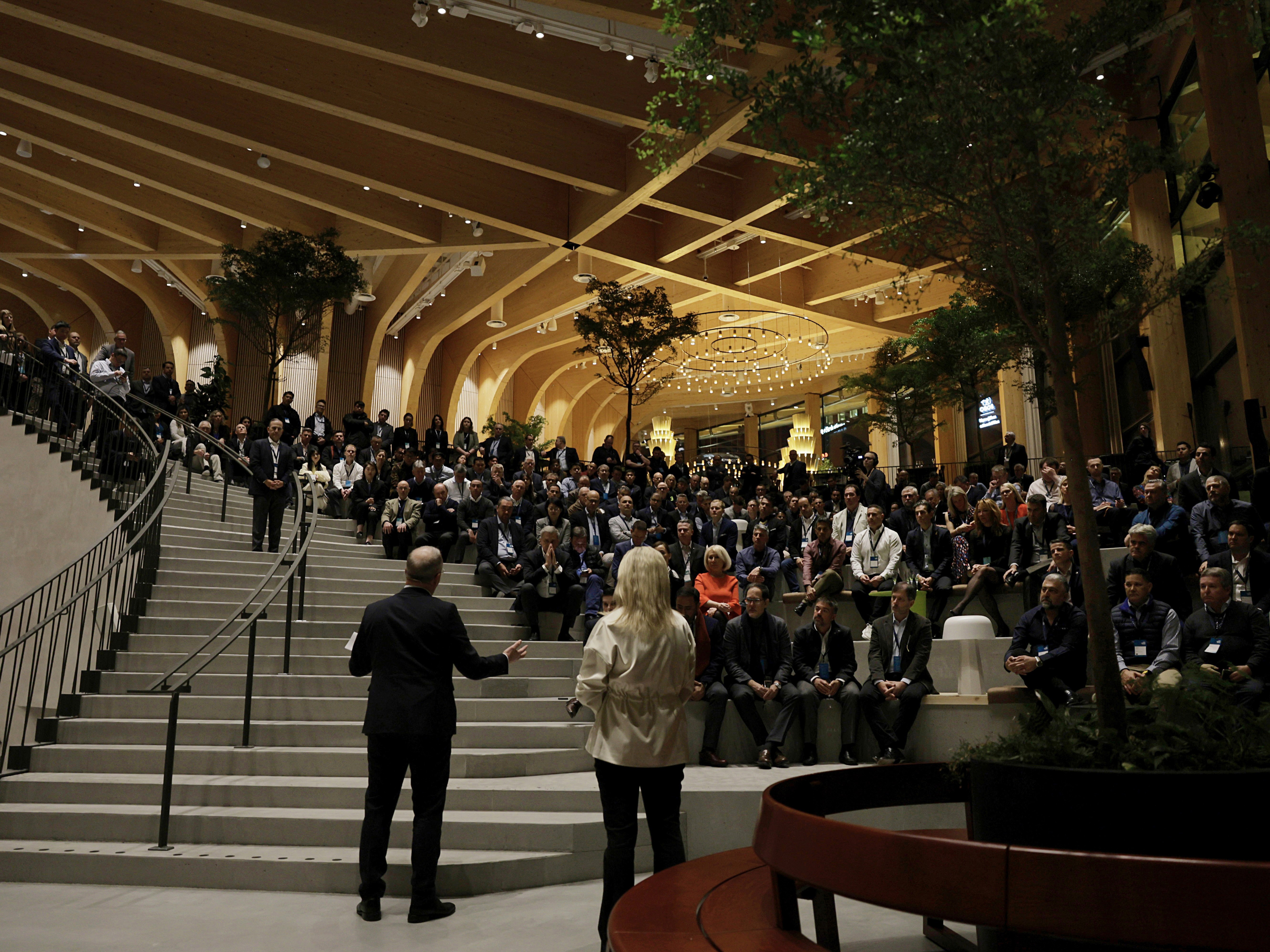 En presentatör talar inför en stor publik, stående på trappan vid World of Volvo