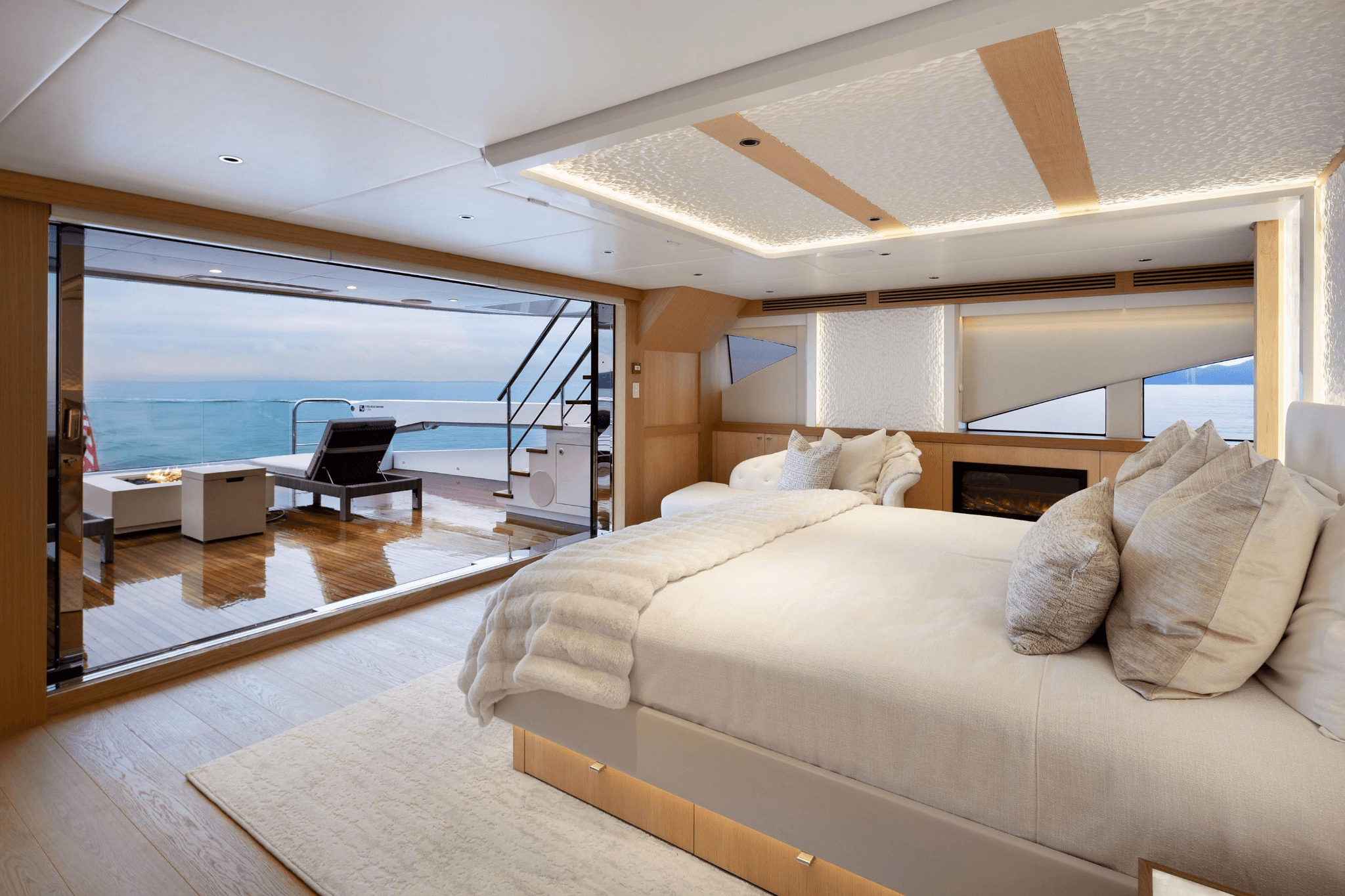 Luxury yacht bedroom opening onto a private deck with ocean views, lounge seating, and a fire feature.