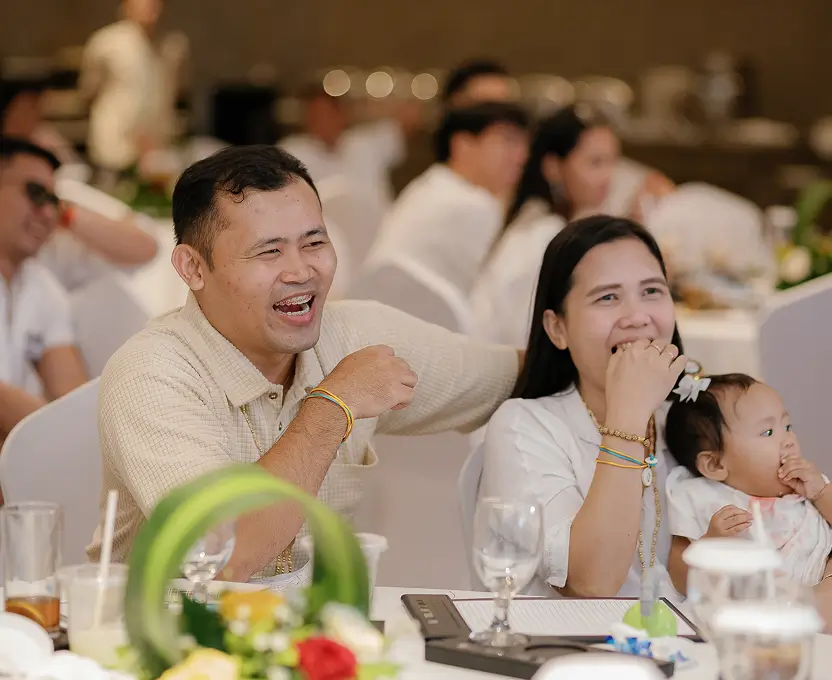 HighCall event attendees laughing together at a banquet table while a mother holds her baby.
