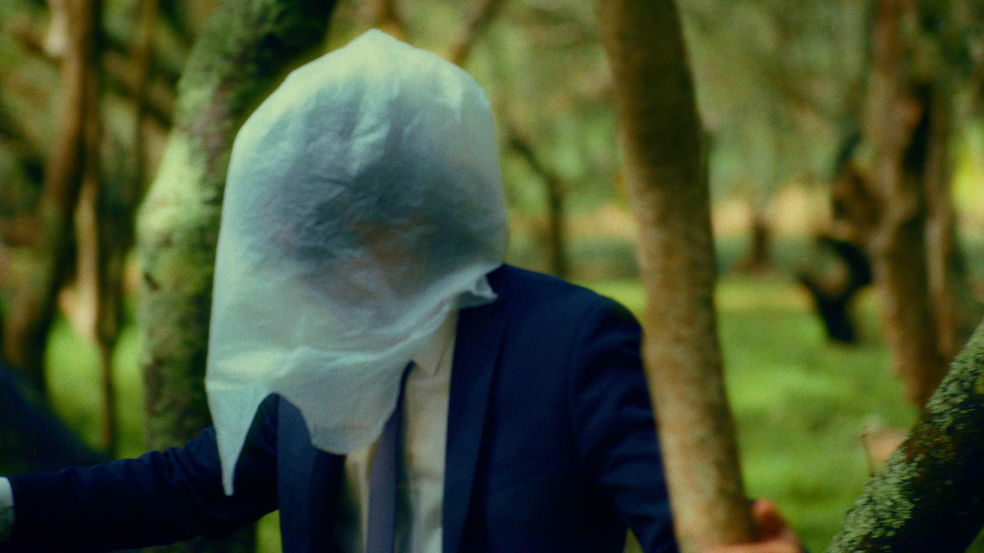 Man with a plastic bag over his head navigates his way through a forest