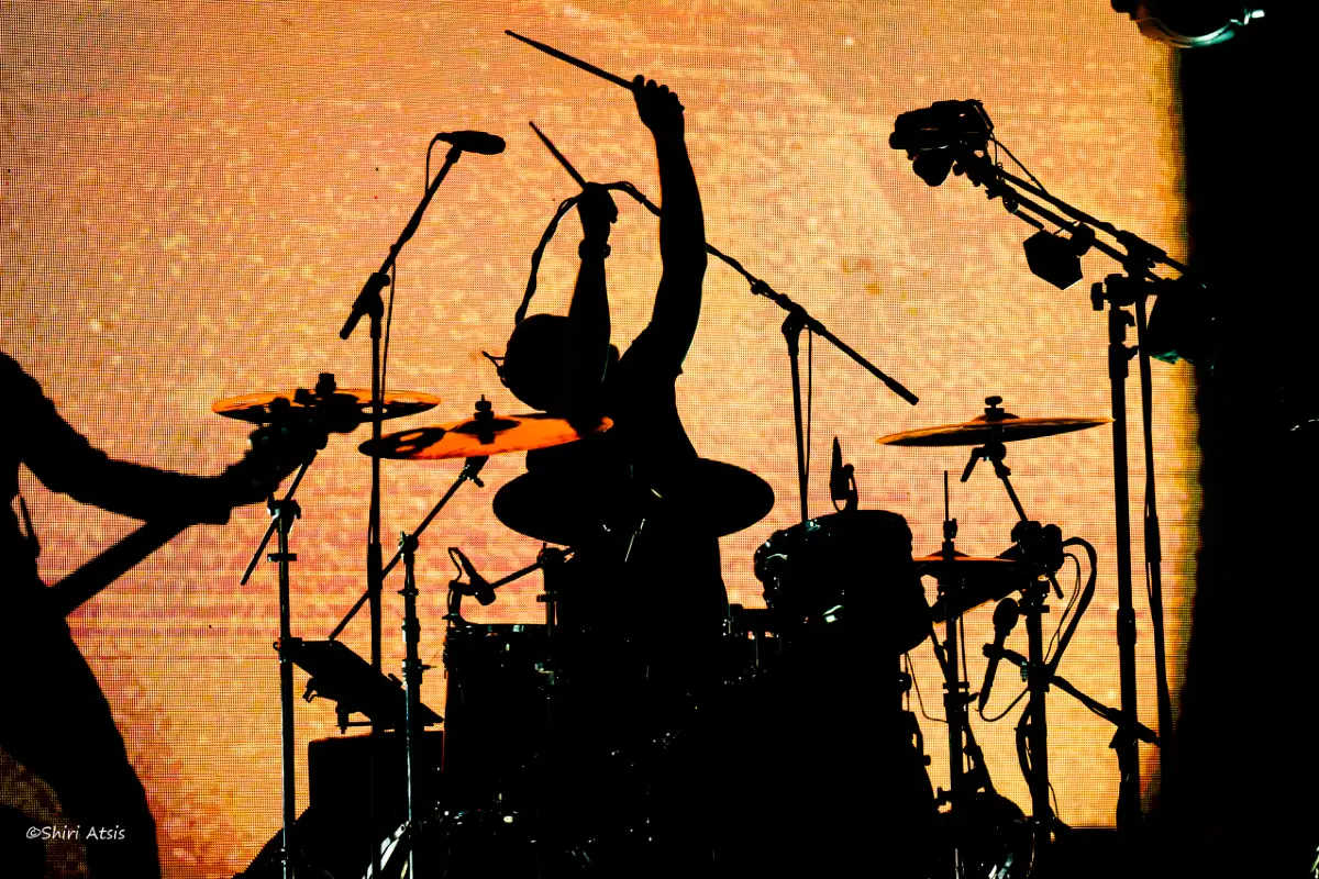 צילום הופעה חיה עוצמתי מאת שירי עציץ - סטודיו Shiriz, ובו צלליות של נגנים על רקע תאורה כתומה חמה וציוד במה מקצועי.