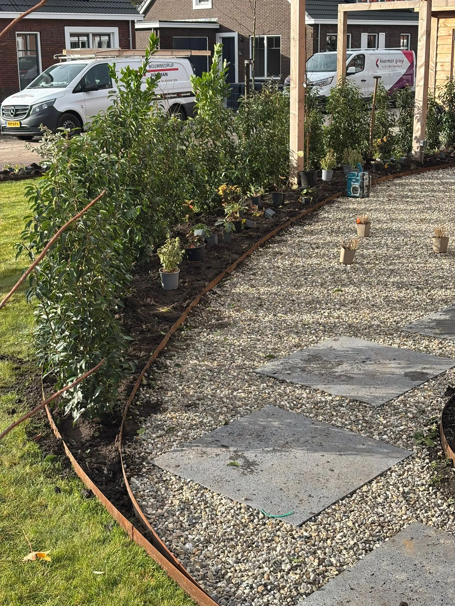 Organisch gevormd grindpad met grote betontegels, jonge struiken langs de rand en een groen gazon ernaast.