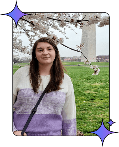 A woman standing next to cherry blossom trees with the Washington Monument in the background.