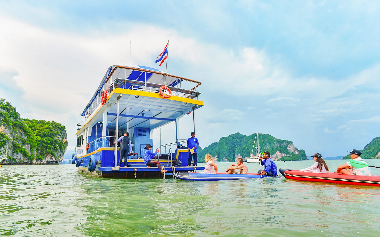 นักท่องเที่ยวพายเรือคายัคใกล้เรือที่อ่าวพังงา โดยมีหน้าผาหินปูนเป็นฉากหลัง