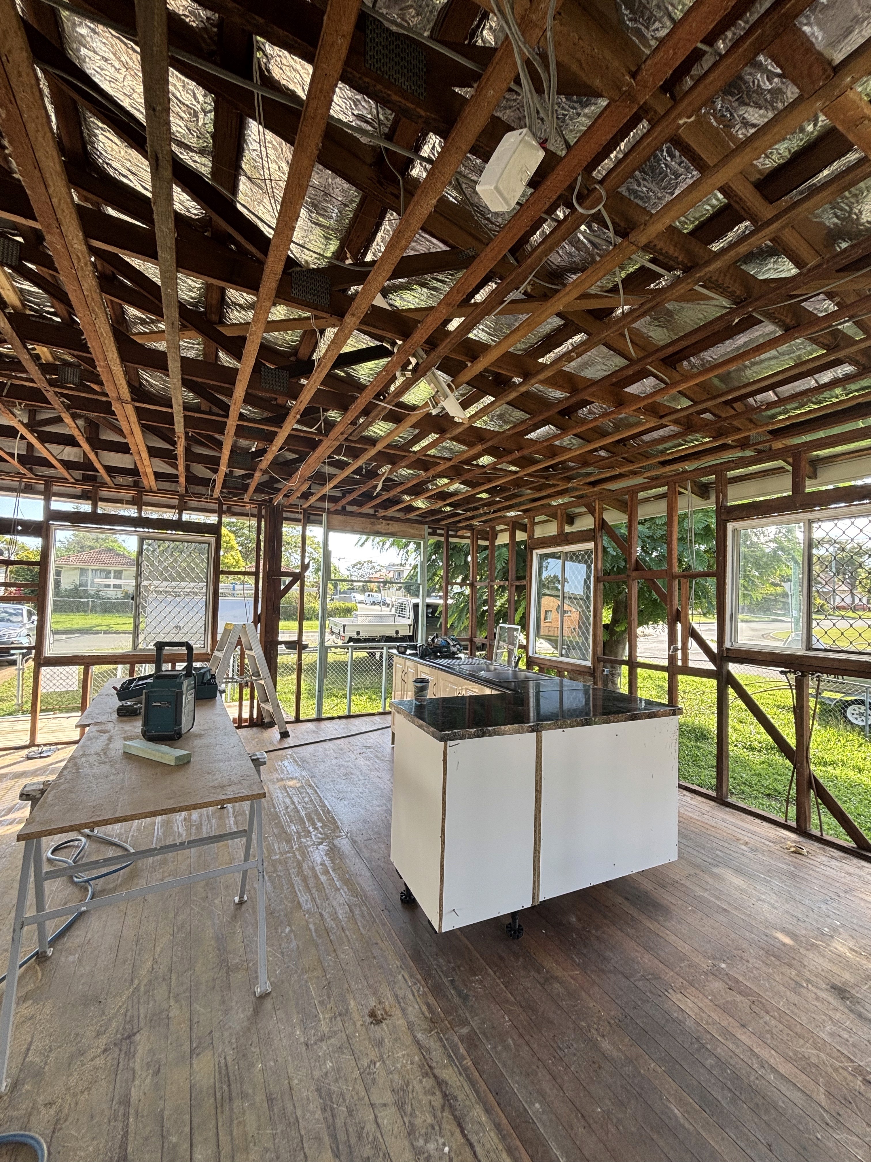 A man and a woman in casual clothing stand face-to-face in a photography studio with a white backdrop. Both have a neutral expression as they engage in conversation.