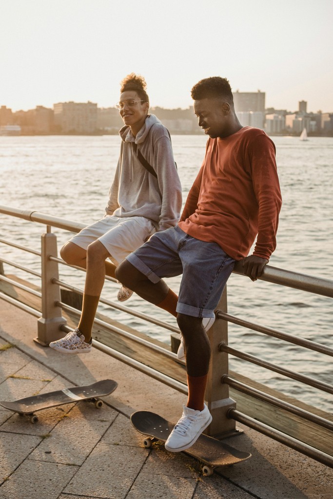 Two young men relaxing by the waterfront during sunset, with skateboards at their feet, enjoying the serene view and each other's company.