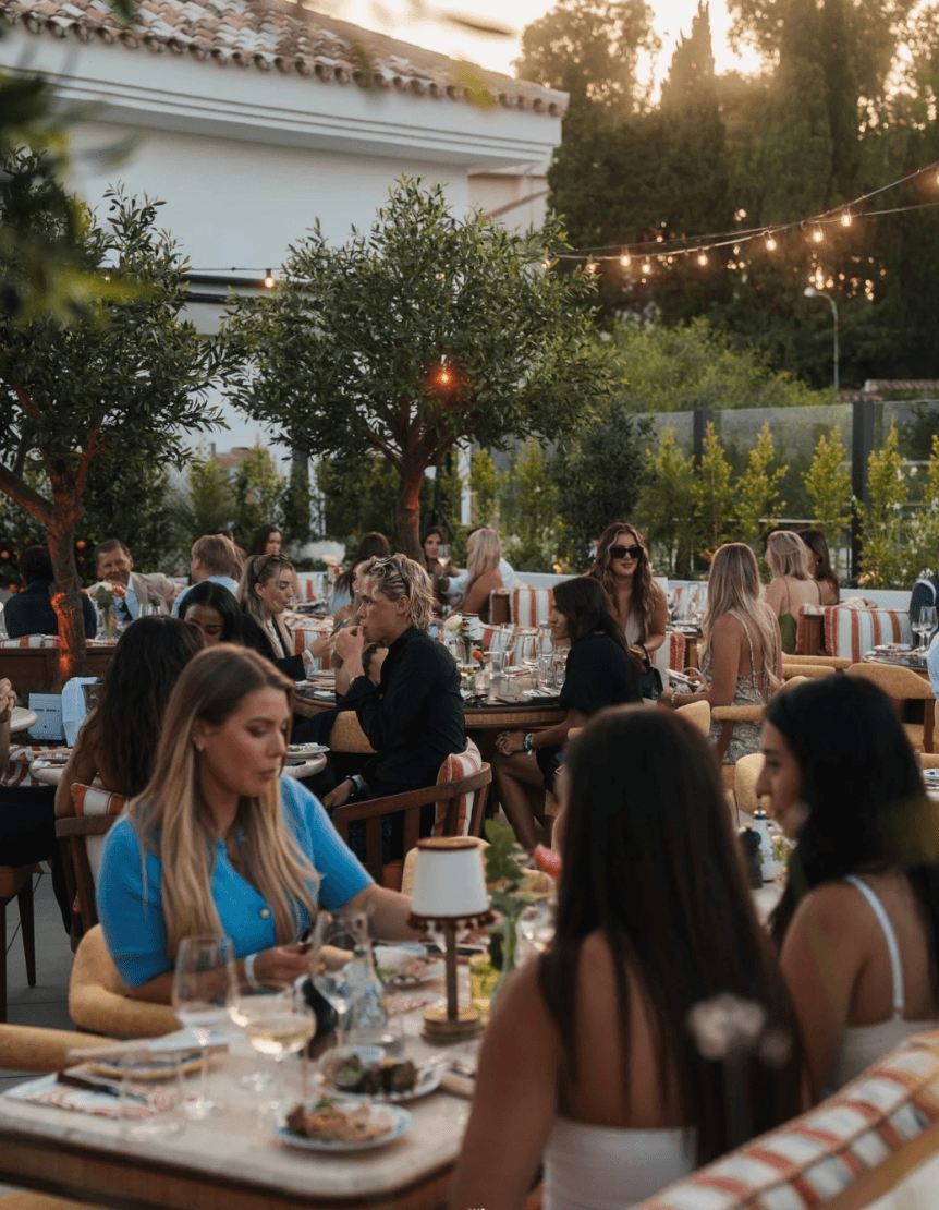 Outdoor lounge under a wooden pergola, draped linen curtains, beige cushions, ocean backdrop, palm shadows dancing on the walls, serene luxury.